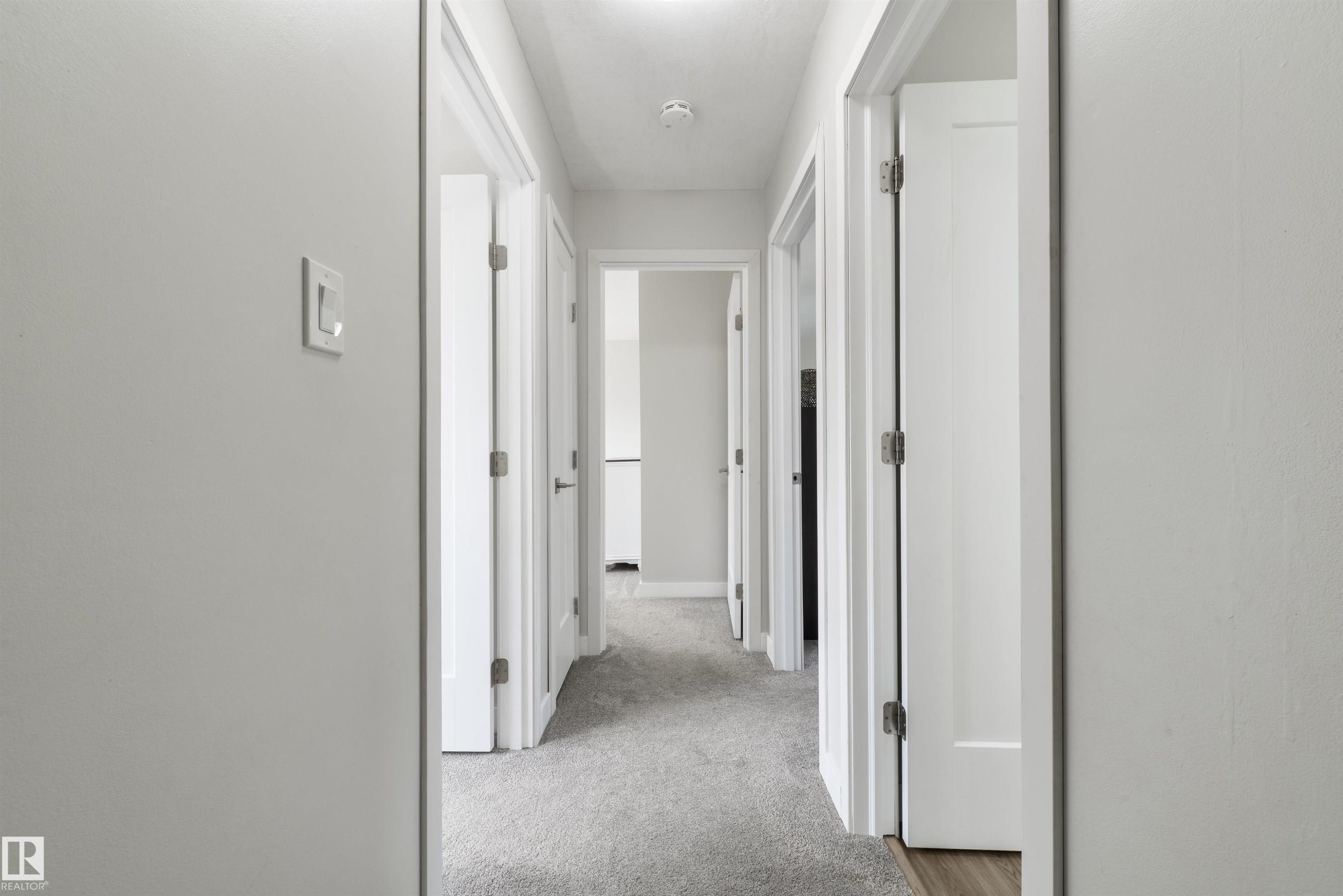 Carpeted hallway featuring multiple white paneled doors and light gray walls - 4614 53 Ave, Calmar, AB - Indoor Photo Showing Other Room