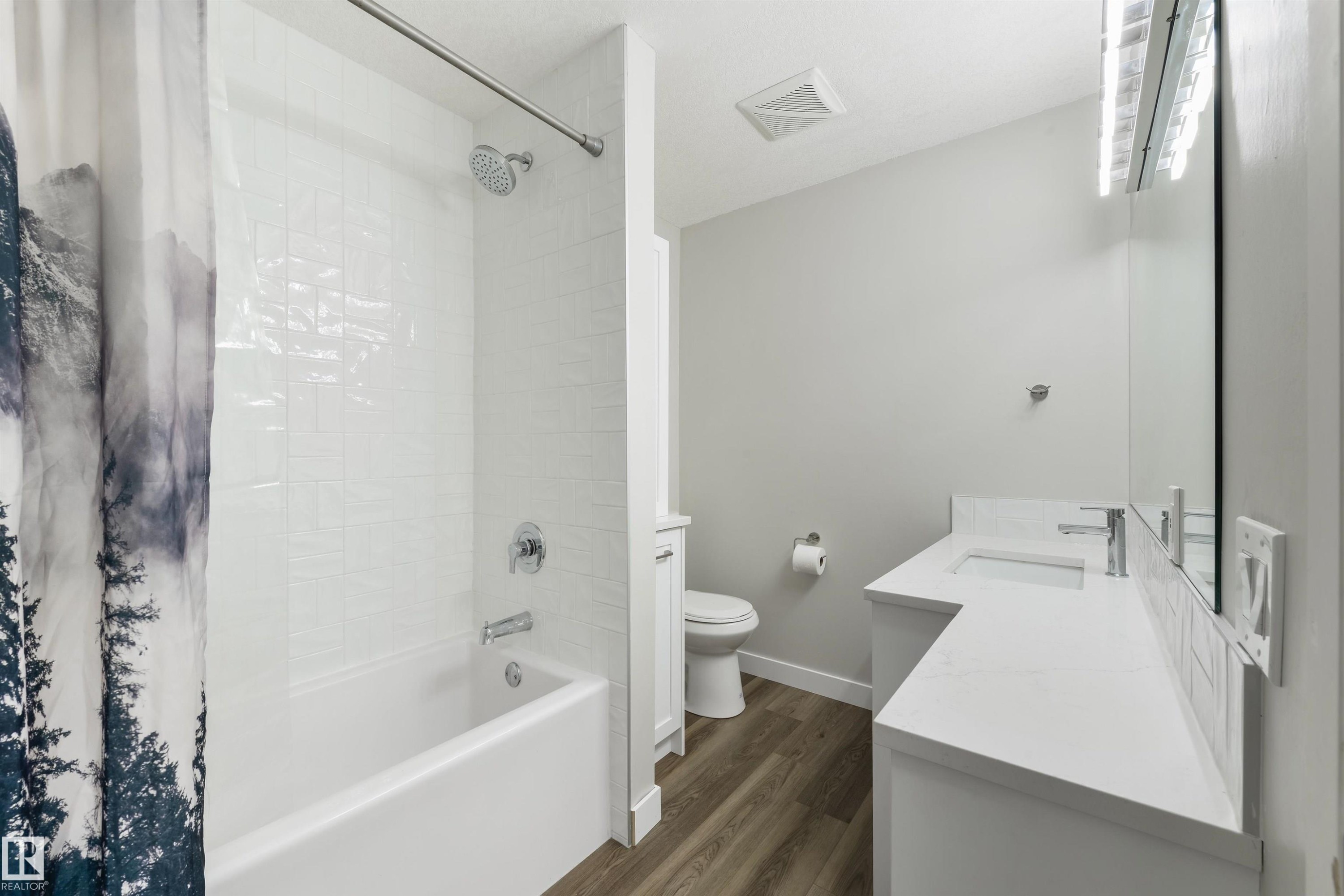 White subway tile shower surround with chrome fixtures, white bathtub, vanity with integrated sink, white countertop, wood-finish flooring - 4614 53 Ave, Calmar, AB - Indoor Photo Showing Bathroom