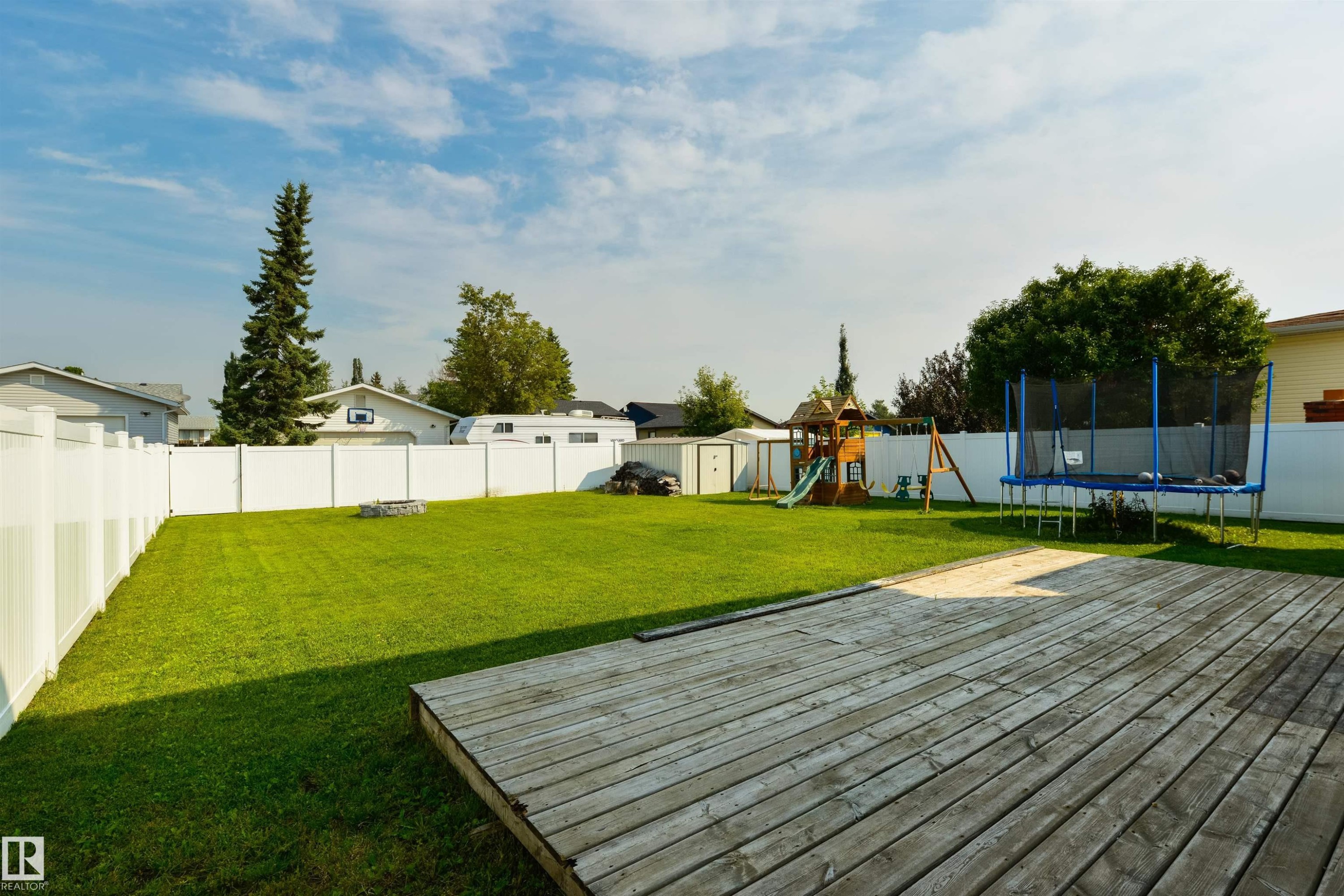 Expansive backyard featuring a wood deck, manicured lawn, and white privacy fencing - 4614 53 Ave, Calmar, AB - Outdoor With Backyard