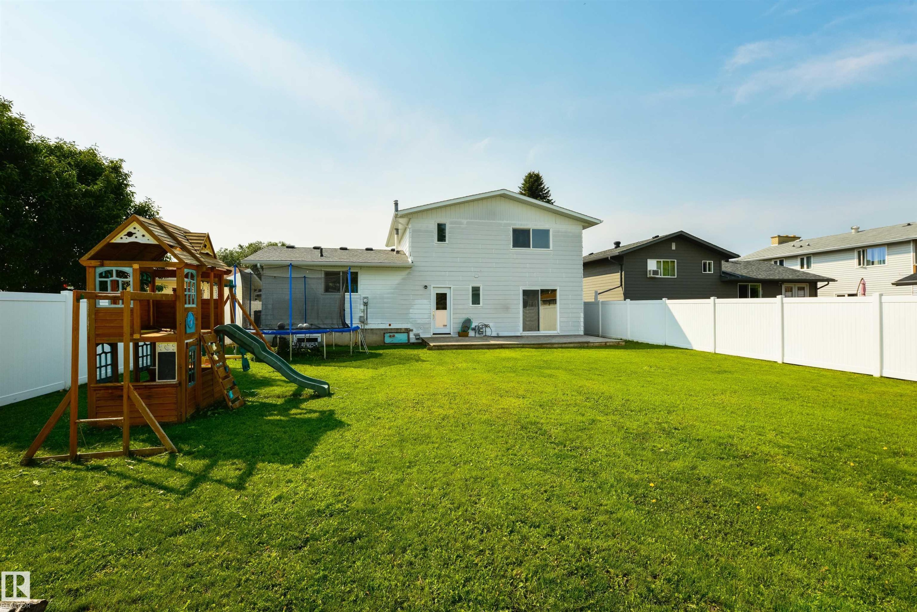 Expansive grassy yard with white privacy fencing and a rear deck - 4614 53 Ave, Calmar, AB - Outdoor With Backyard With Exterior