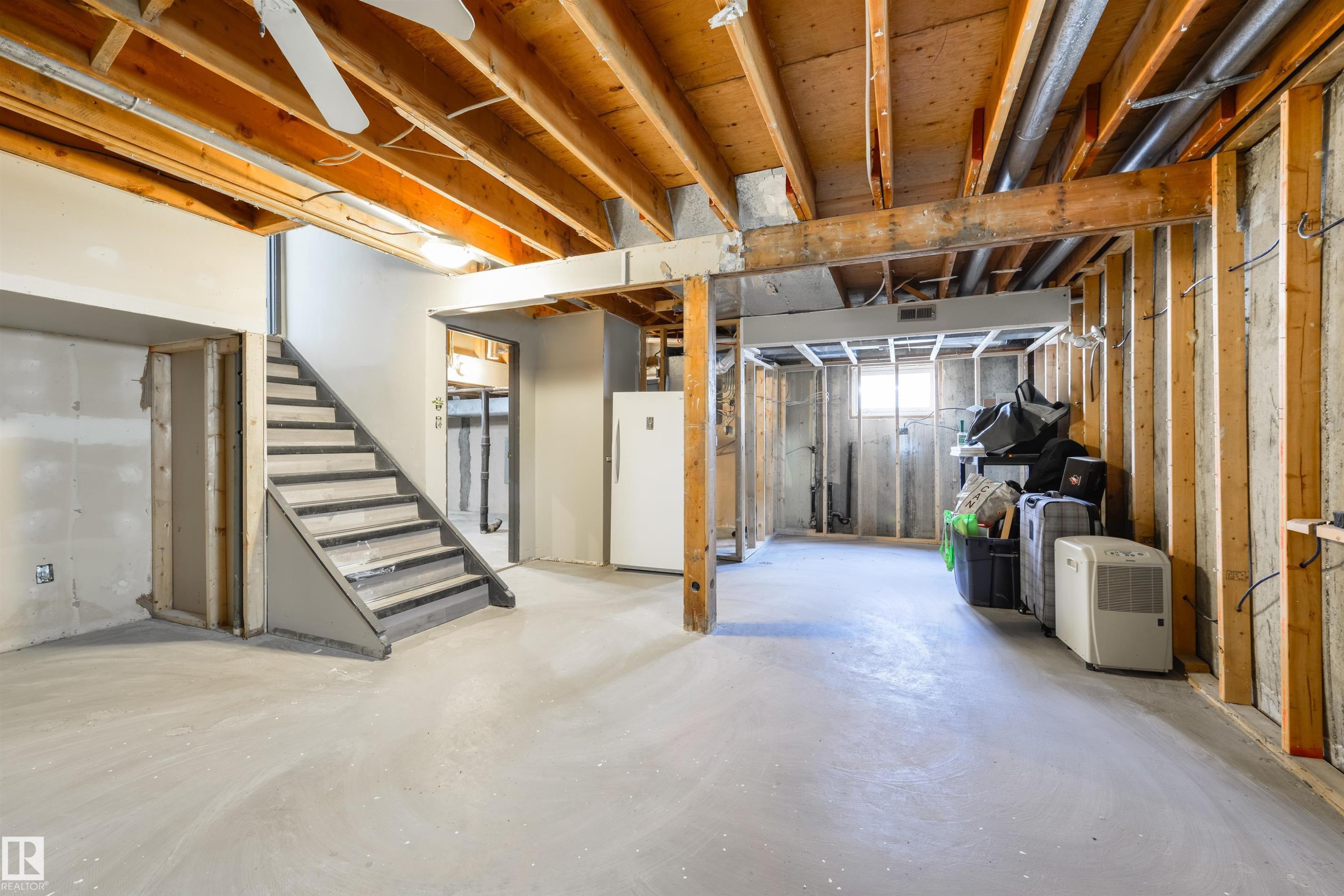 Unfinished basement with exposed wood joists and framing, a staircase with painted risers, and concrete flooring - 4614 53 Ave, Calmar, AB - Indoor Photo Showing Basement