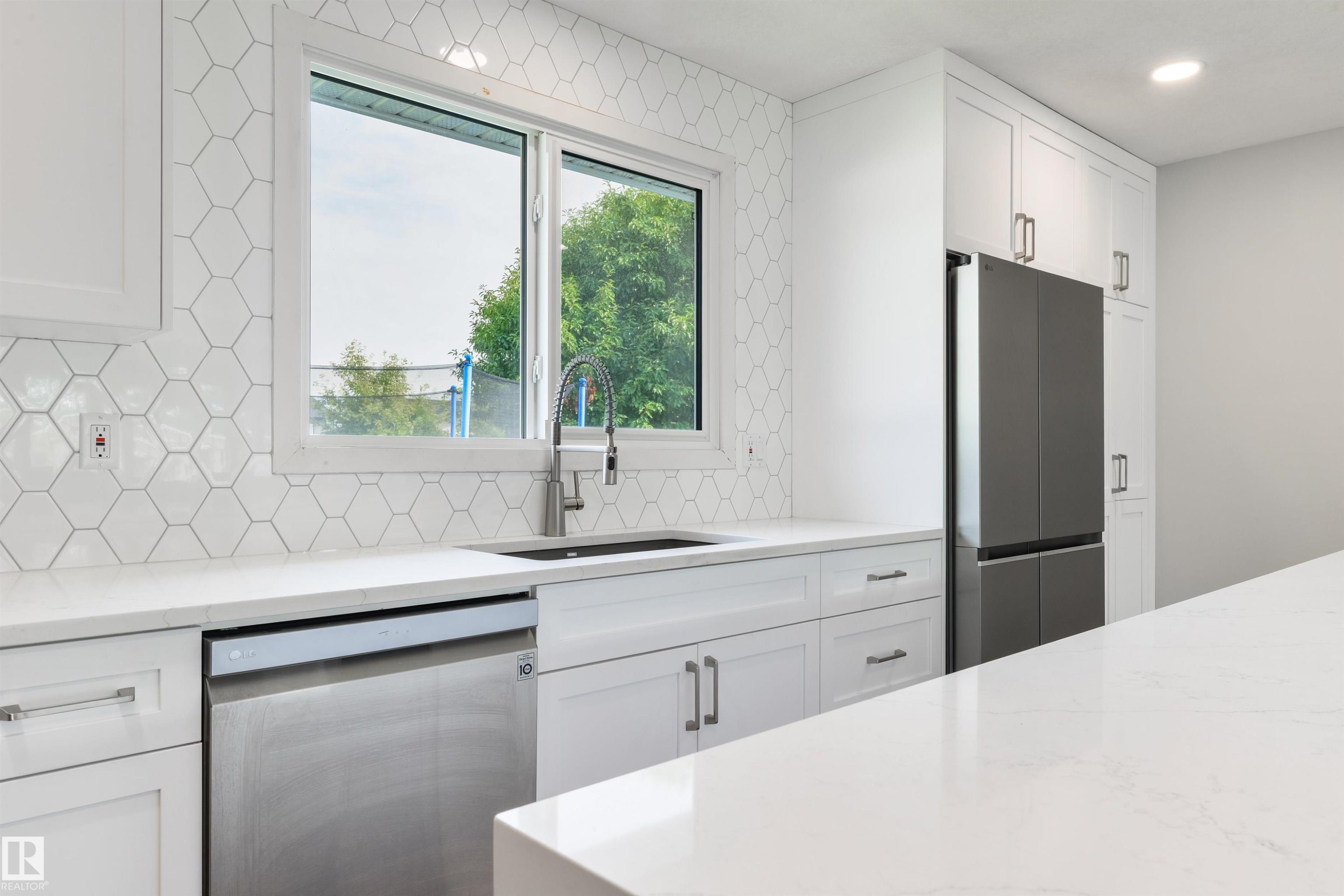 White shaker-style cabinetry, quartz countertops, hexagonal tile backsplash, stainless steel appliances, and an undermount sink with a gooseneck faucet - 4614 53 Ave, Calmar, AB - Indoor Photo Showing Kitchen