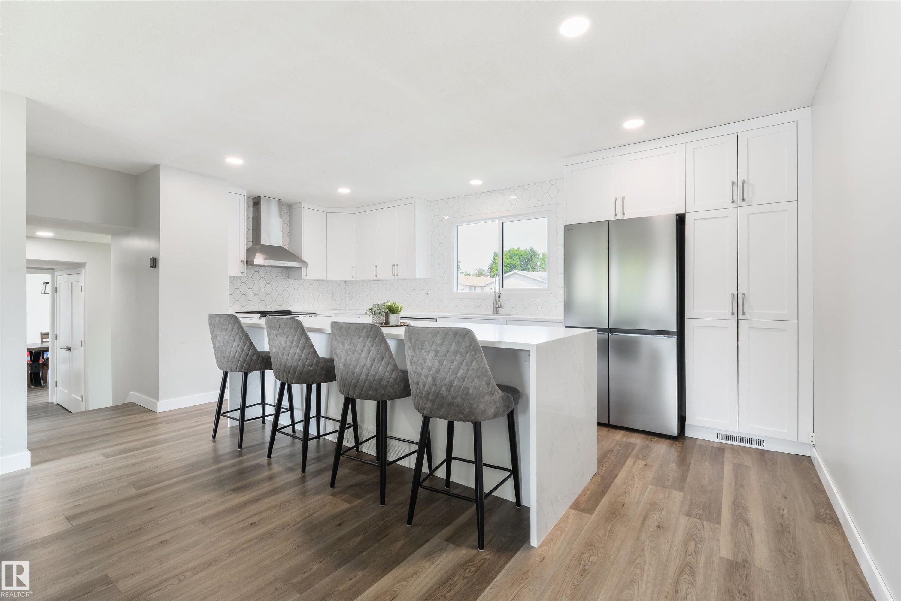 Modern kitchen featuring an island with seating, stainless steel appliances, extensive white cabinetry, and wood-finish flooring - 4614 53 Ave, Calmar, AB - Indoor Photo Showing Kitchen With Upgraded Kitchen