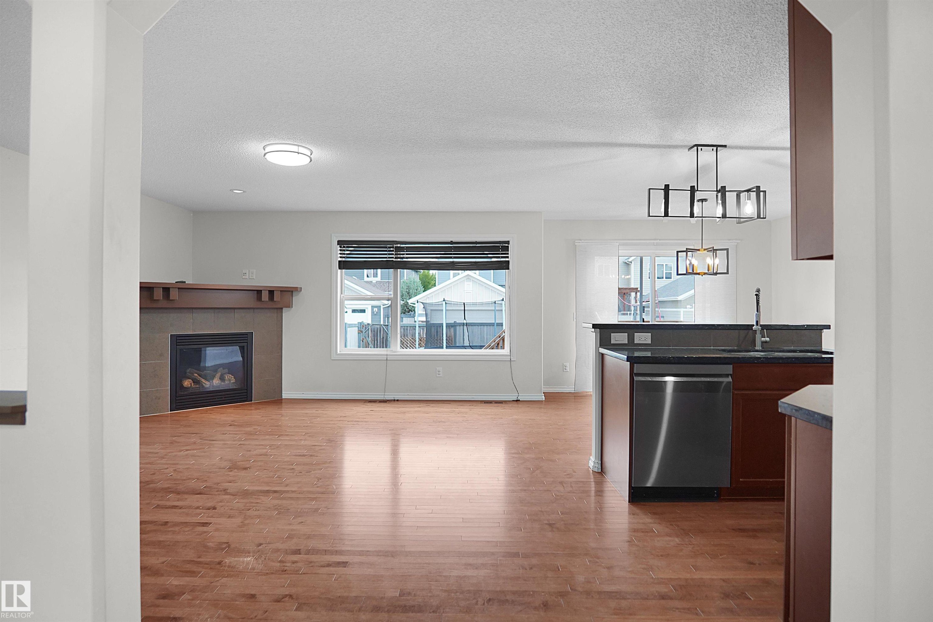 Hardwood-finish flooring, built-in fireplace with stone surround and wood mantel, stainless steel dishwasher, and contemporary chandelier - 8432 18 Avenue Sw, Edmonton, AB - Indoor With Fireplace