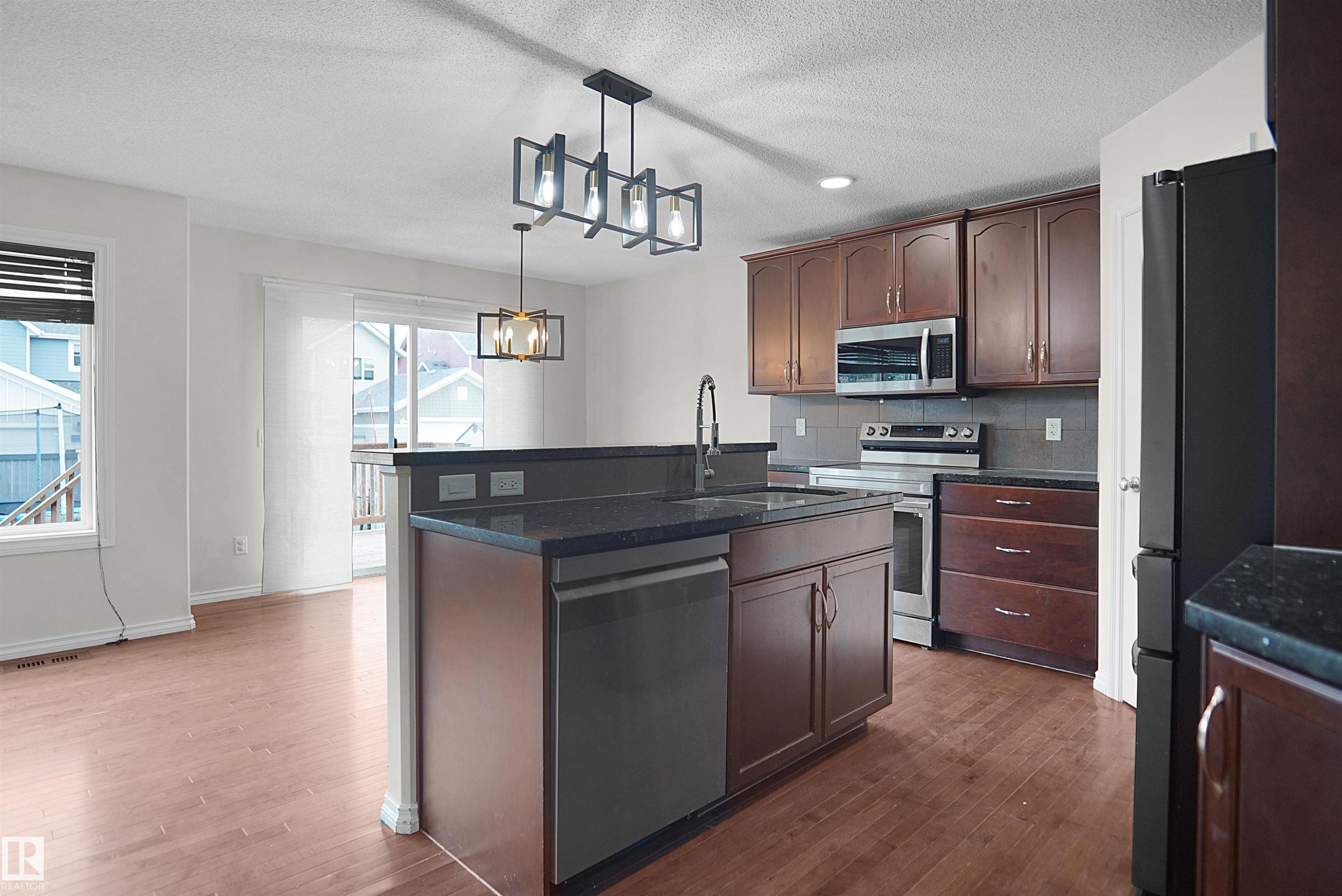 Kitchen featuring a central island with an integrated sink, dark cabinetry, and stainless steel appliances - 8432 18 Avenue Sw, Edmonton, AB - Indoor Photo Showing Kitchen