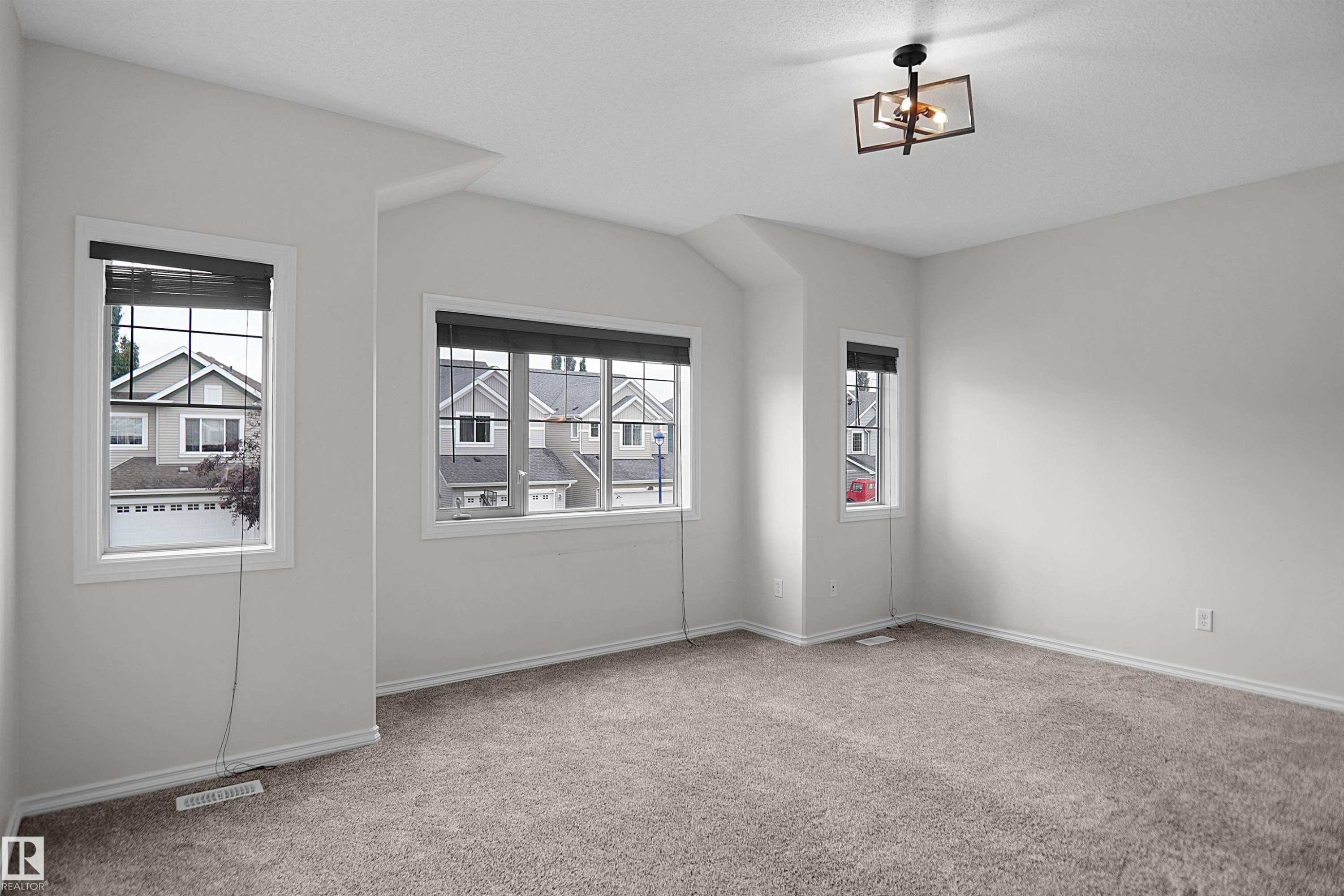 Neutral wall paint, light-colored carpet flooring, multiple windows, and a contemporary ceiling light fixture - 8432 18 Avenue Sw, Edmonton, AB - Indoor Photo Showing Other Room