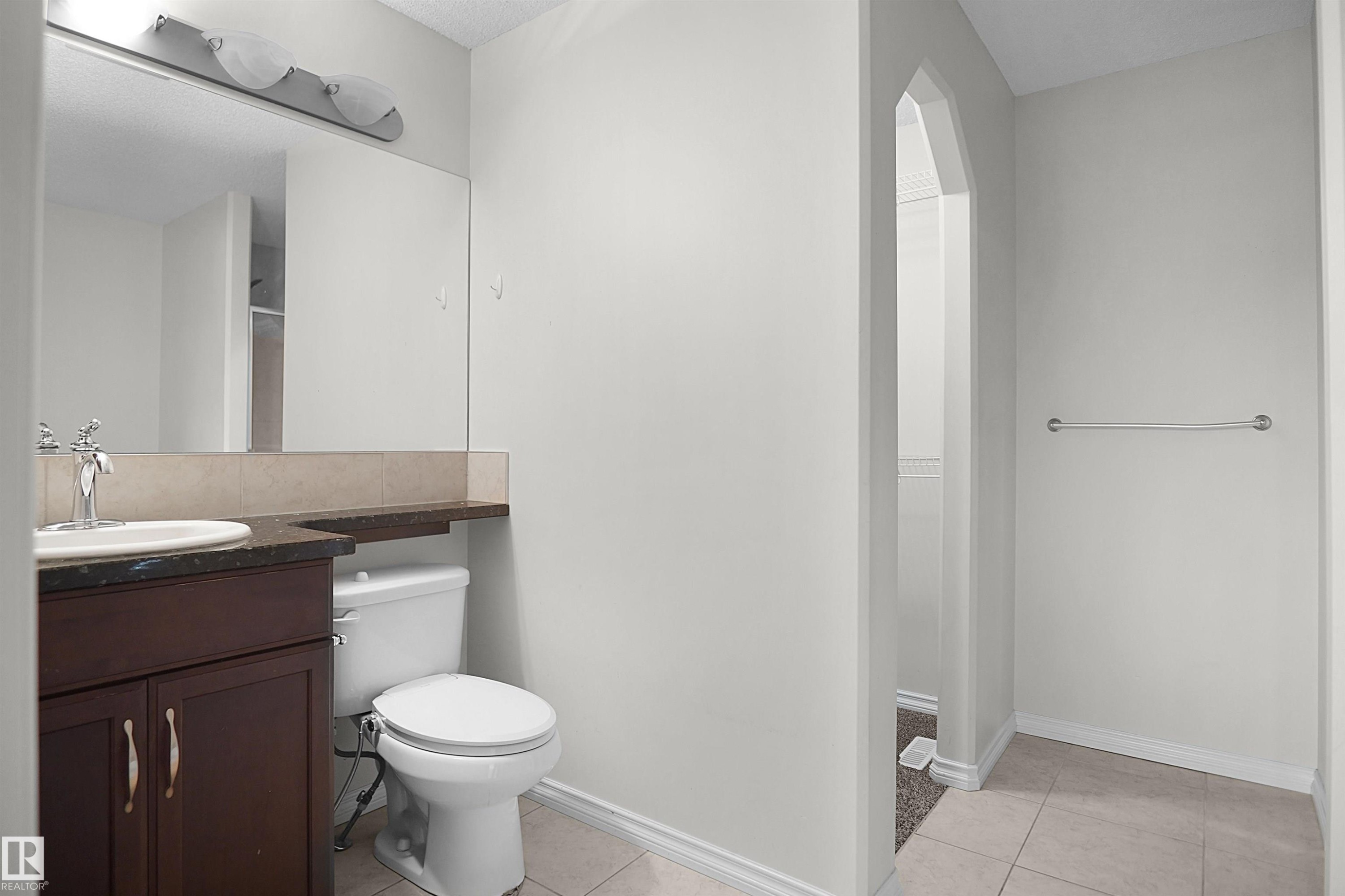 Dark wood-finish vanity with a single basin sink, dark stone-finish countertop, and full-width mirror - 8432 18 Avenue Sw, Edmonton, AB - Indoor Photo Showing Bathroom