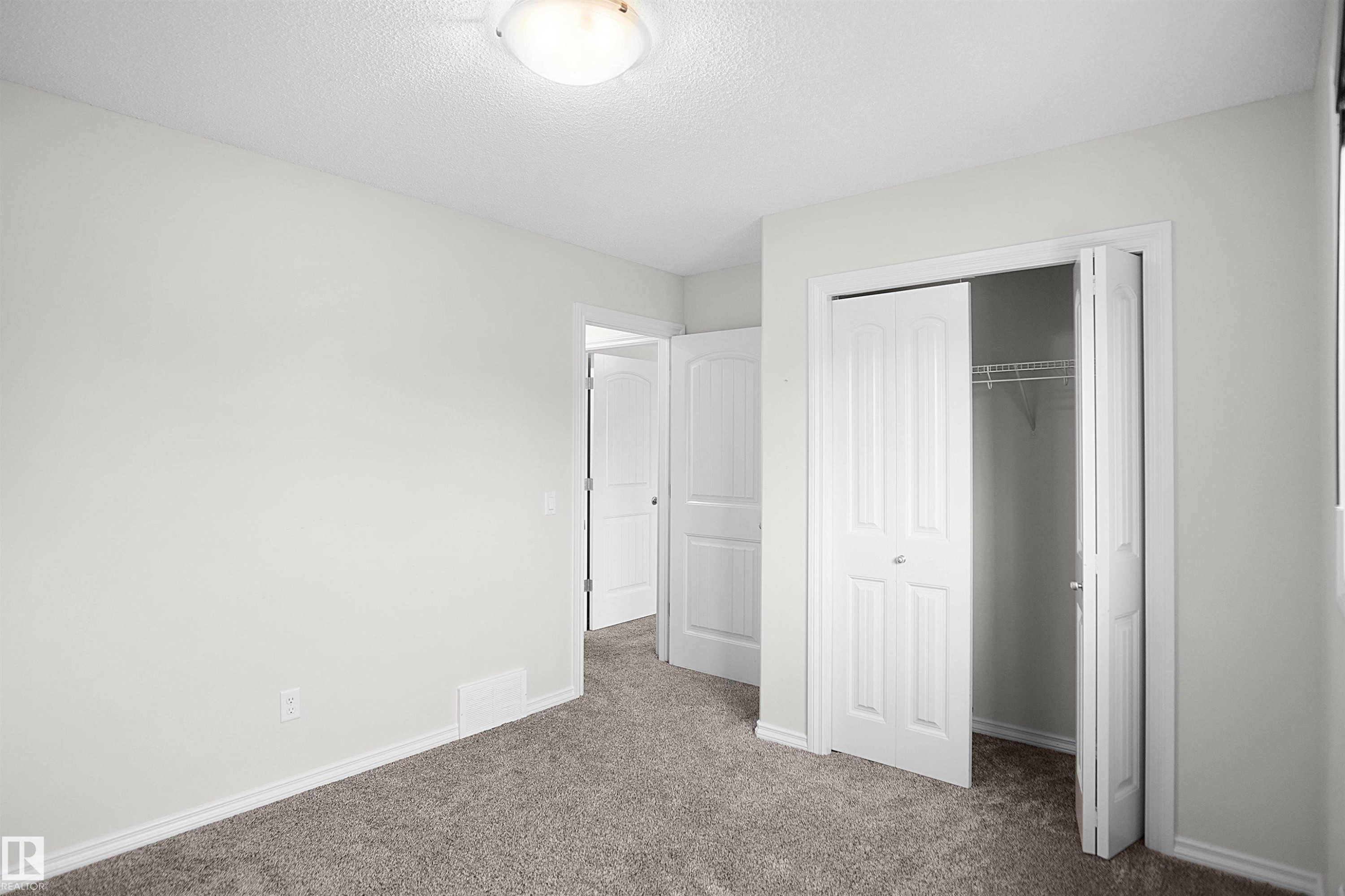 Plush gray carpeting, neutral wall palette, white trim, and bi-fold closet doors with wire shelving - 8432 18 Avenue Sw, Edmonton, AB - Indoor