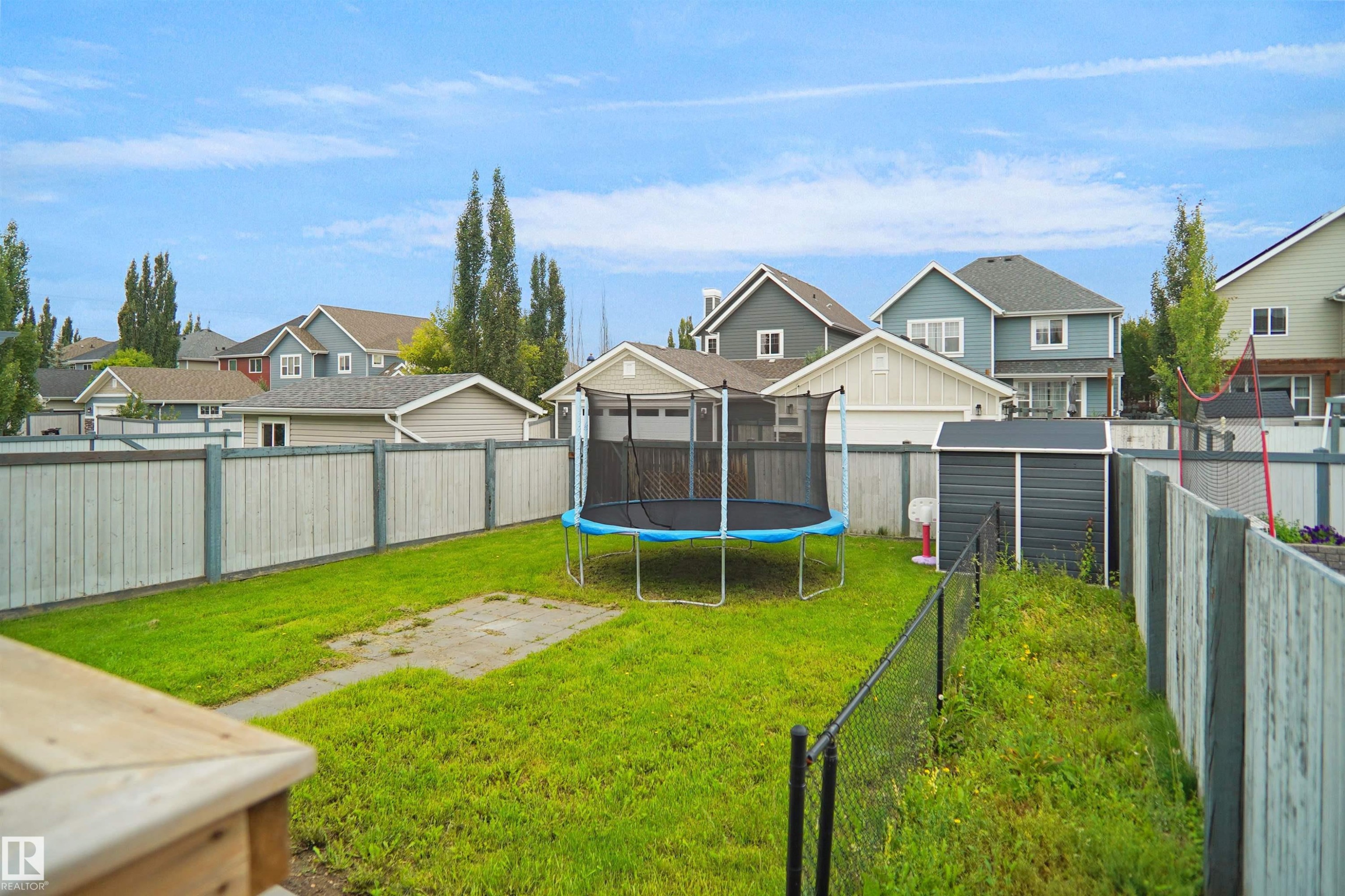 Expansive backyard oasis featuring a large trampoline, manicured lawn, mature poplar trees, and metal fencing - 8432 18 Avenue Sw, Edmonton, AB - Outdoor