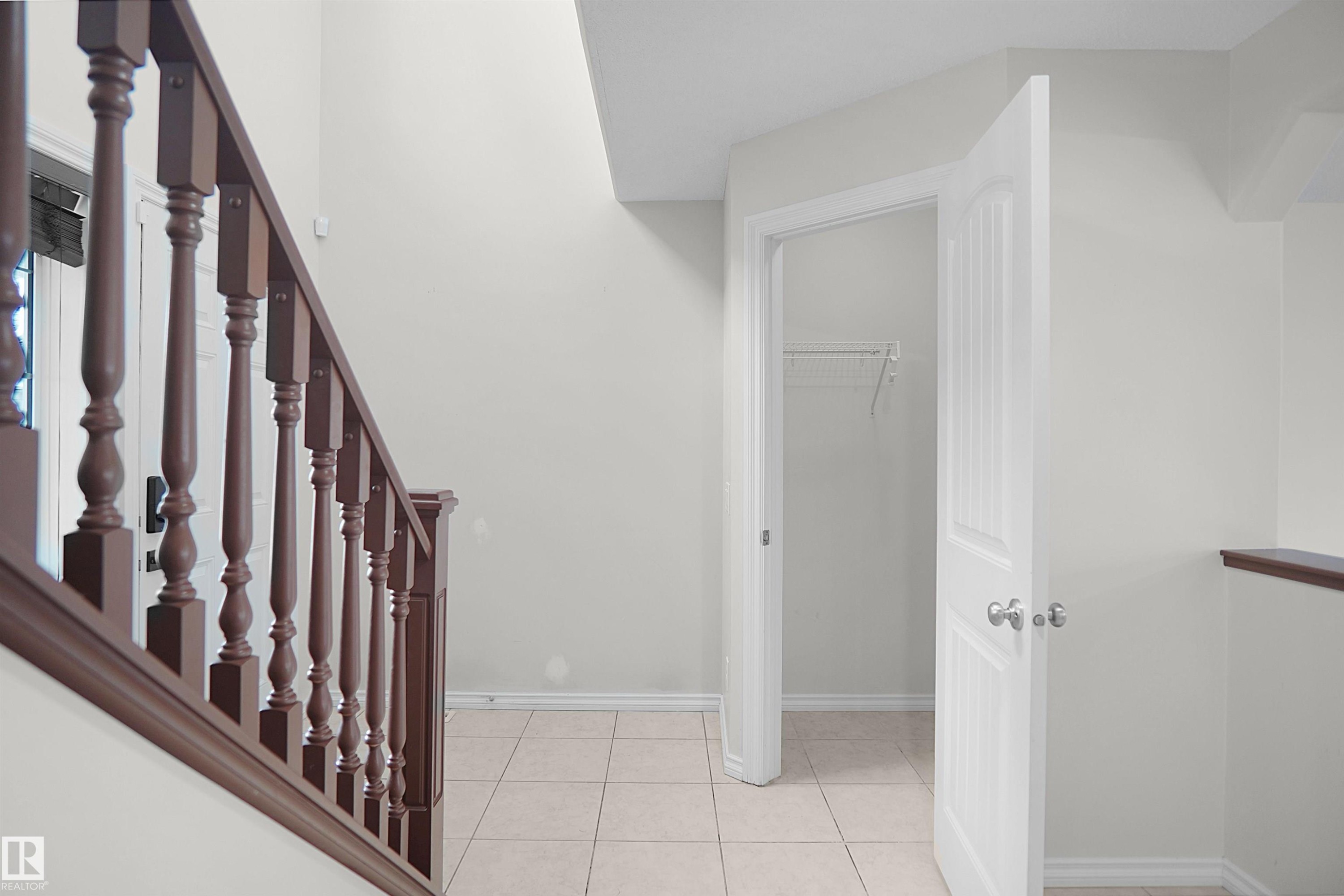 Tiled flooring with contrasting baseboards, painted walls, and a wooden stair railing - 8432 18 Avenue Sw, Edmonton, AB - Indoor Photo Showing Other Room