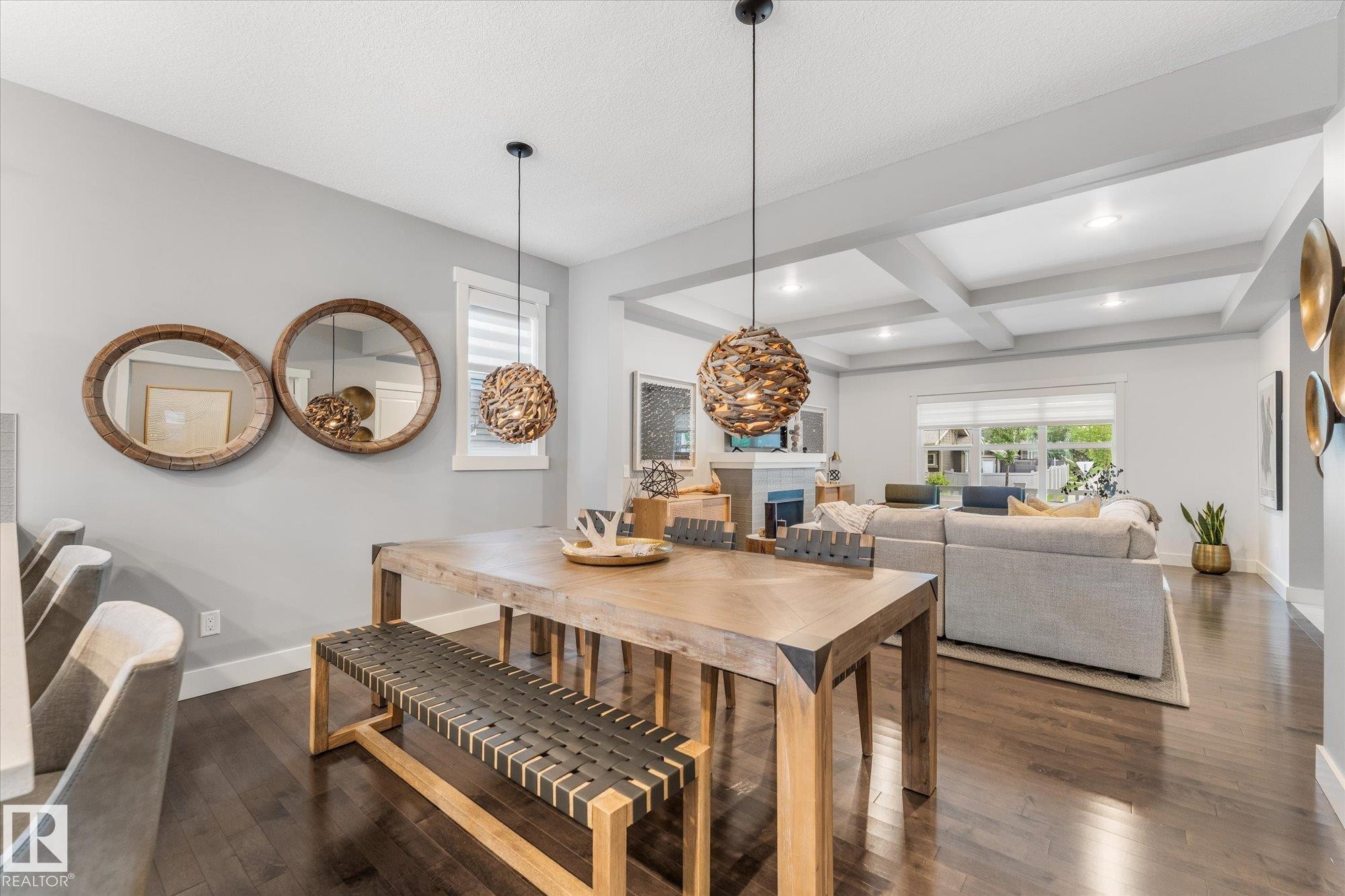 Open-concept dining and living area featuring a wood-finish dining table with matching bench seating, pendant lighting with woven natural-fiber shades, coffered ceiling with recessed lighting, and hardwood flooring throughout - 5616 Juchli Avenue Nw, Edmonton, AB - Indoor Photo Showing Other Room With Fireplace