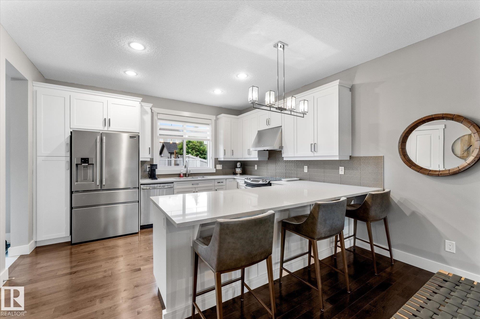 Modern kitchen featuring white cabinetry, stainless steel French-door refrigerator with ice and water dispensers, and a large center island with white quartz countertop and seating for multiple guests - 5616 Juchli Avenue Nw, Edmonton, AB - Indoor Photo Showing Kitchen With Upgraded Kitchen