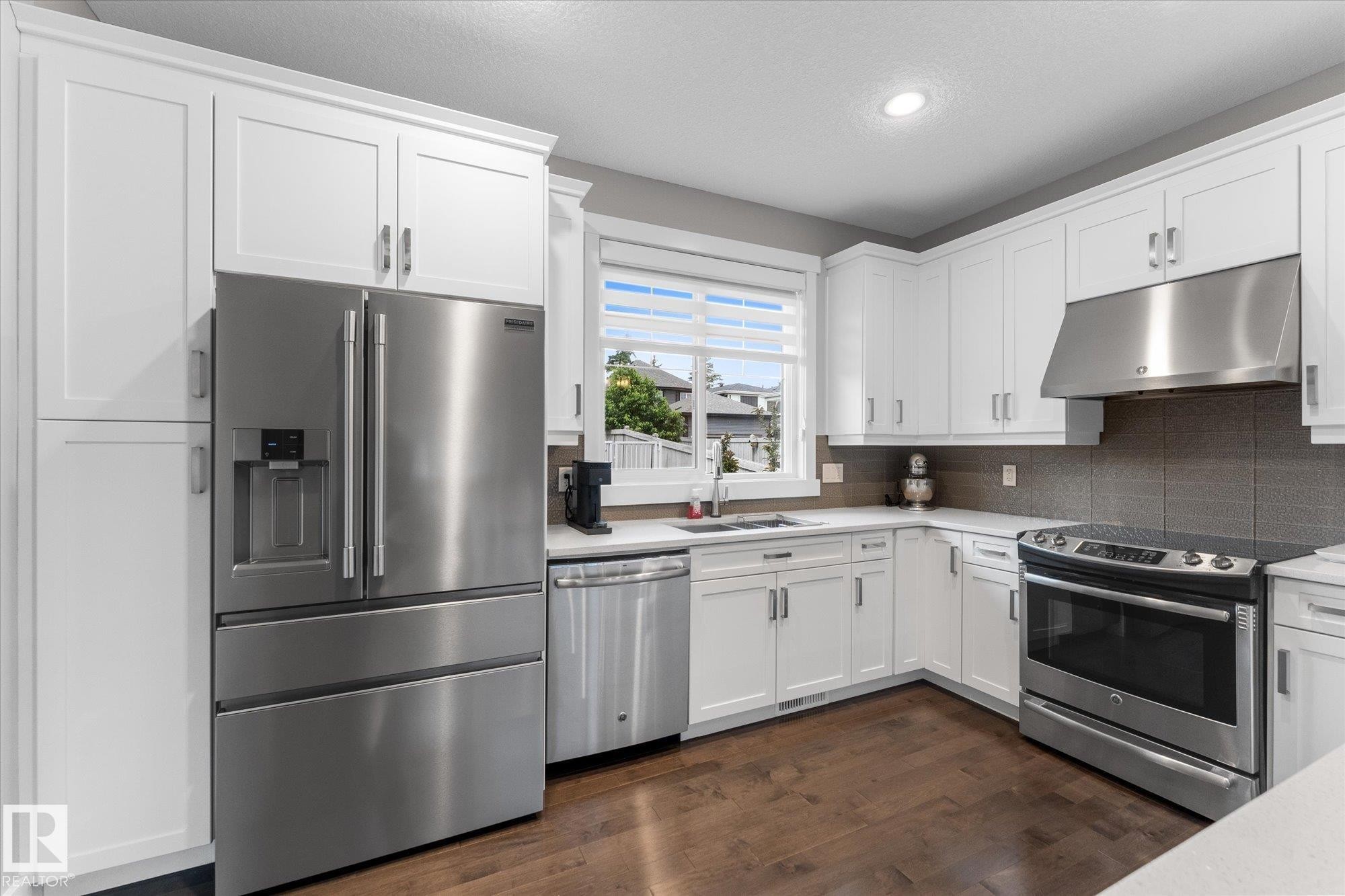 Kitchen with white cabinetry, stainless steel appliances, wood-finish flooring, and light-toned countertops - 5616 Juchli Avenue Nw, Edmonton, AB - Indoor Photo Showing Kitchen