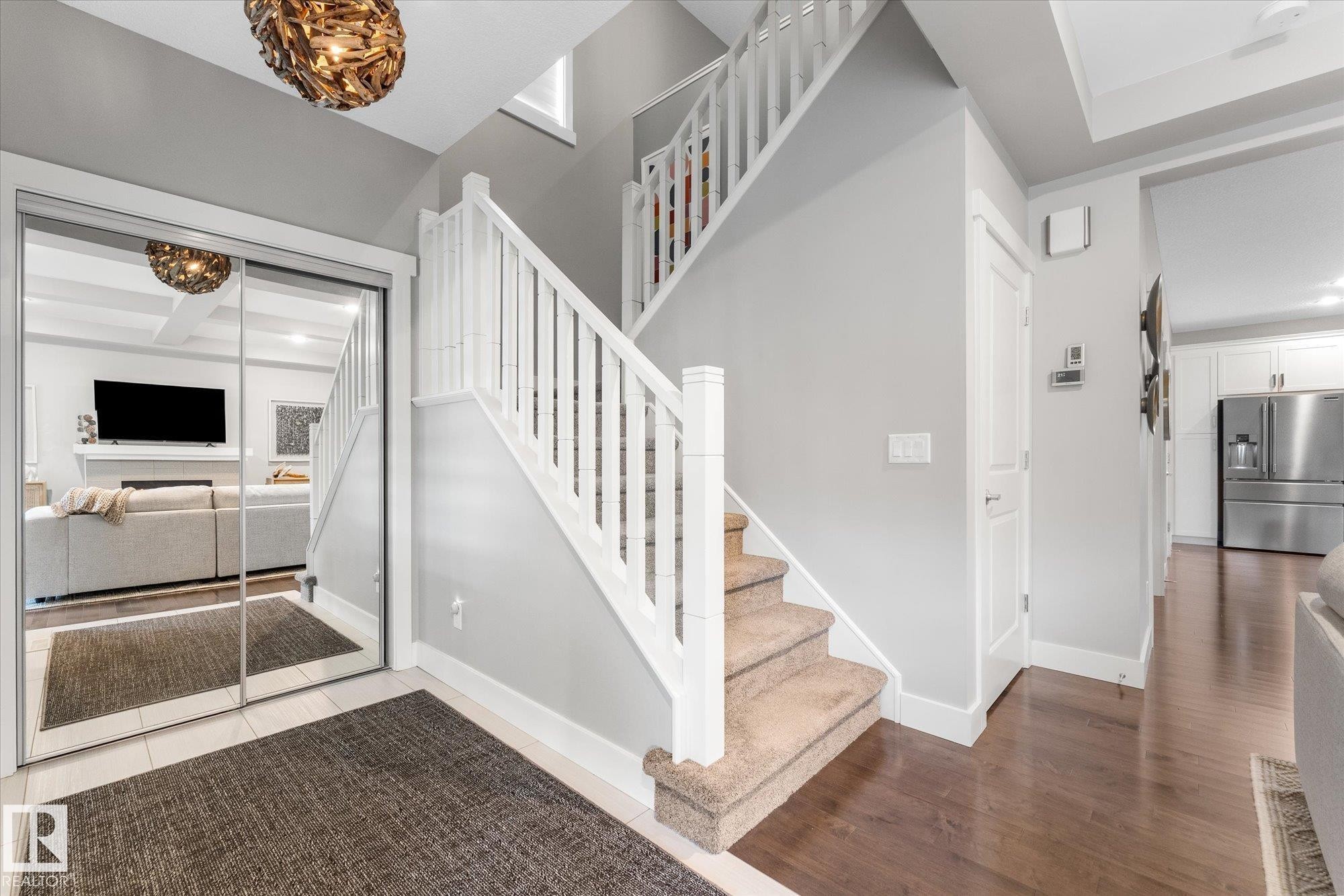 Mirrored closet doors, hardwood flooring, white staircase railing, carpeted stairs, and a decorative light fixture - 5616 Juchli Avenue Nw, Edmonton, AB - Indoor Photo Showing Other Room