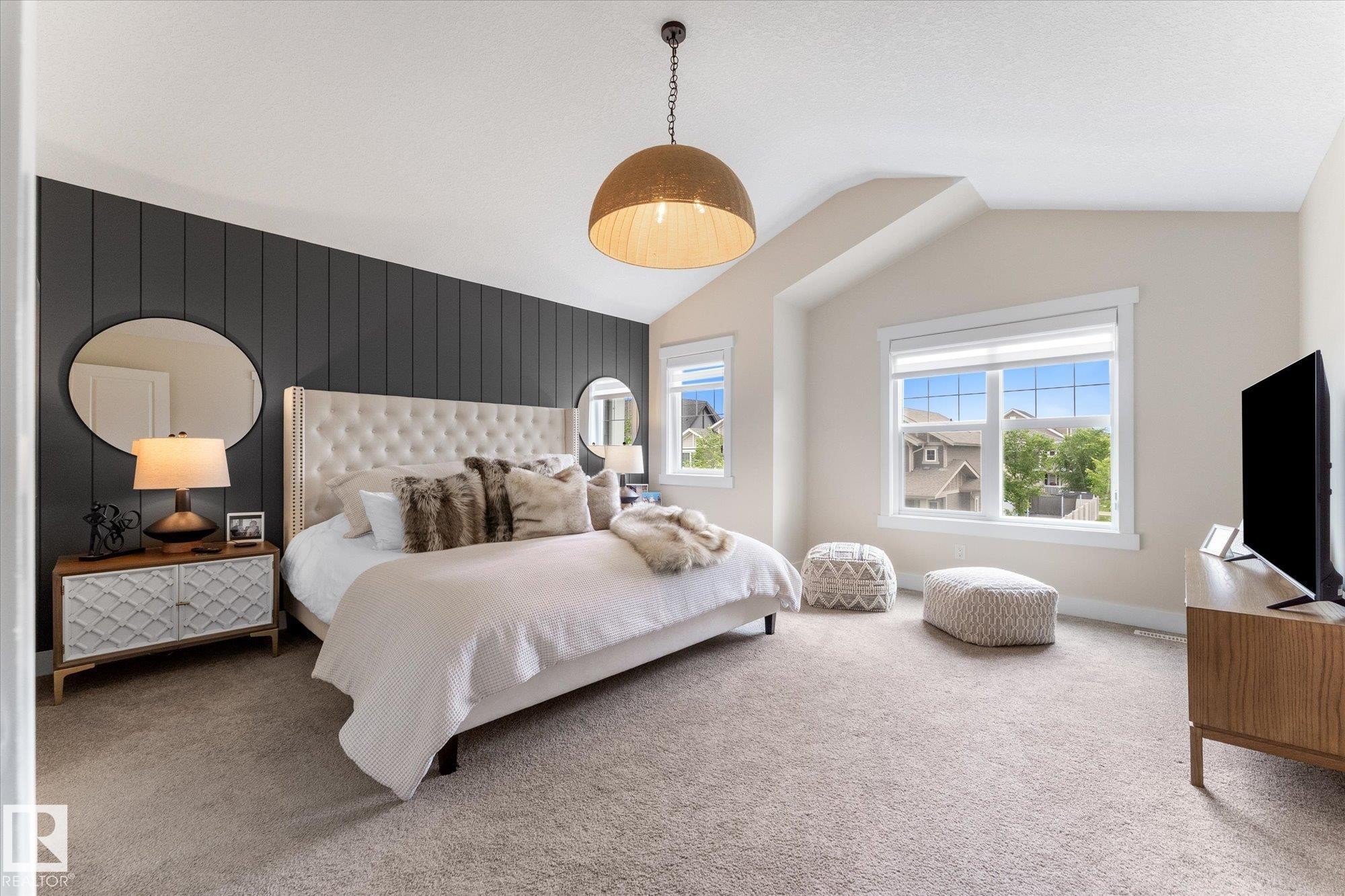 Spacious primary bedroom featuring a tufted upholstered headboard, pendant lighting, and abundant natural light from oversized windows - 5616 Juchli Avenue Nw, Edmonton, AB - Indoor Photo Showing Bedroom