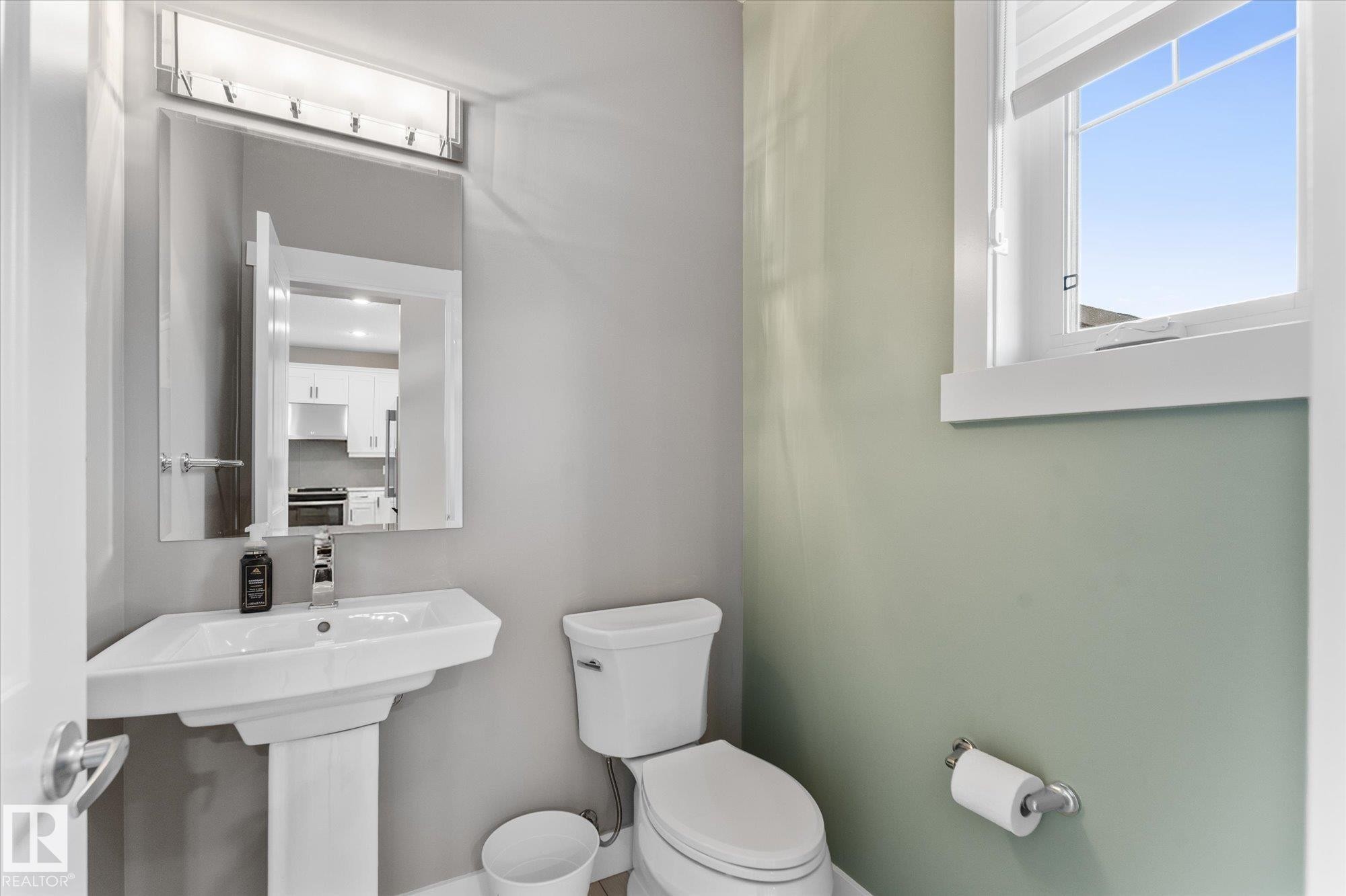 White pedestal sink, modern wall-mounted faucet, and rectangular mirror with overhead lighting - 5616 Juchli Avenue Nw, Edmonton, AB - Indoor Photo Showing Bathroom