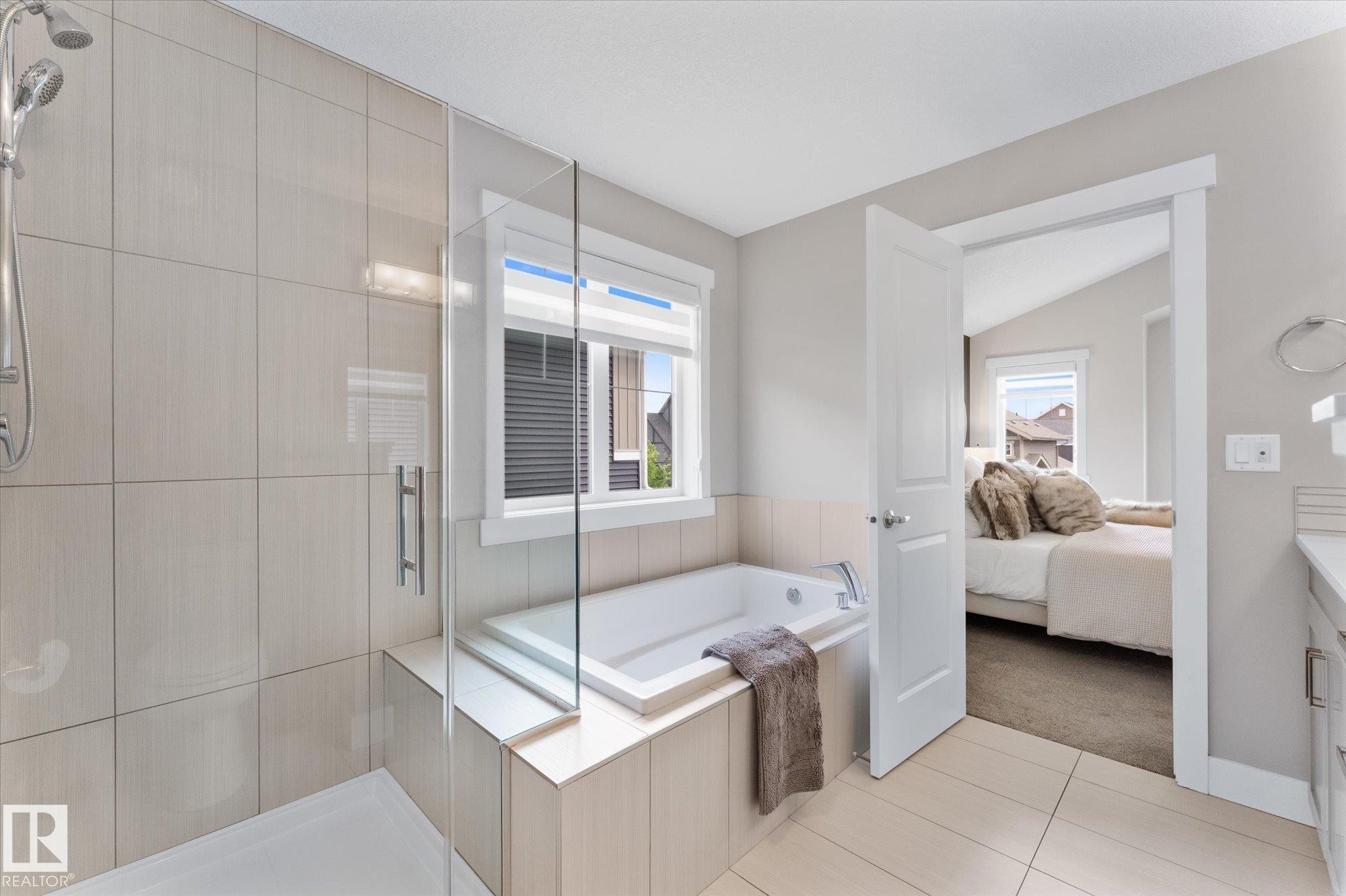 Spa-inspired primary bathroom featuring a frameless glass-enclosed shower with subway tile surround, a freestanding soaking tub positioned beneath a transom window, dual vanities with quartz countertops, and neutral tile flooring throughout - 5616 Juchli Avenue Nw, Edmonton, AB - Indoor