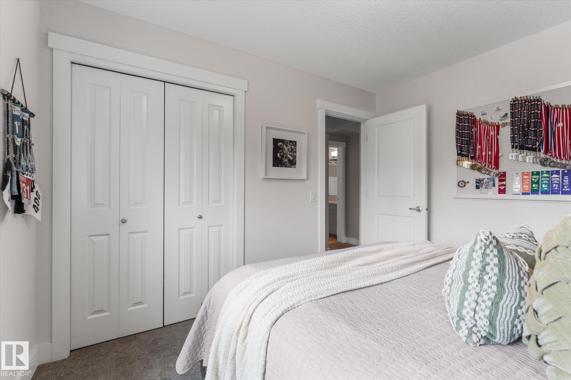 Bright secondary bedroom featuring white six-panel closet doors, neutral carpeting, and clean white walls with simple trim detailing - 5616 Juchli Avenue Nw, Edmonton, AB - Indoor Photo Showing Bedroom