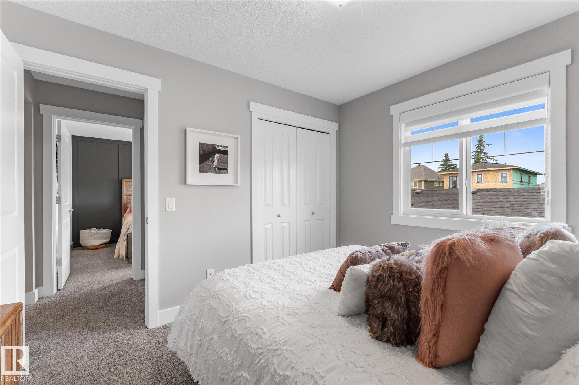 Bright secondary bedroom featuring gray carpeting, white trim and closet doors, and large dual-pane windows with natural light - 5616 Juchli Avenue Nw, Edmonton, AB - Indoor Photo Showing Bedroom