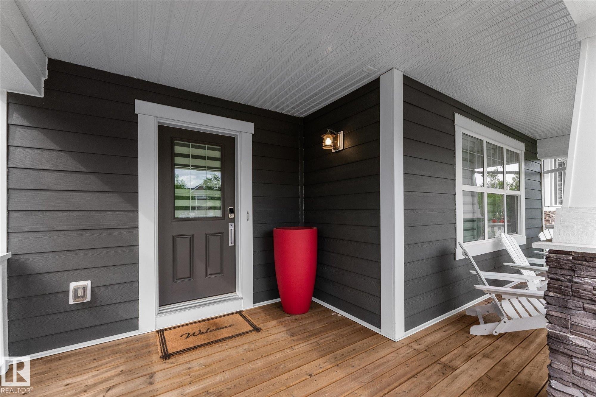 Welcoming front entry featuring a dark horizontal-plank exterior with white trim, six-panel entry door with transom window, and warm wood-finish flooring - 5616 Juchli Avenue Nw, Edmonton, AB - Outdoor With Deck Patio Veranda With Exterior
