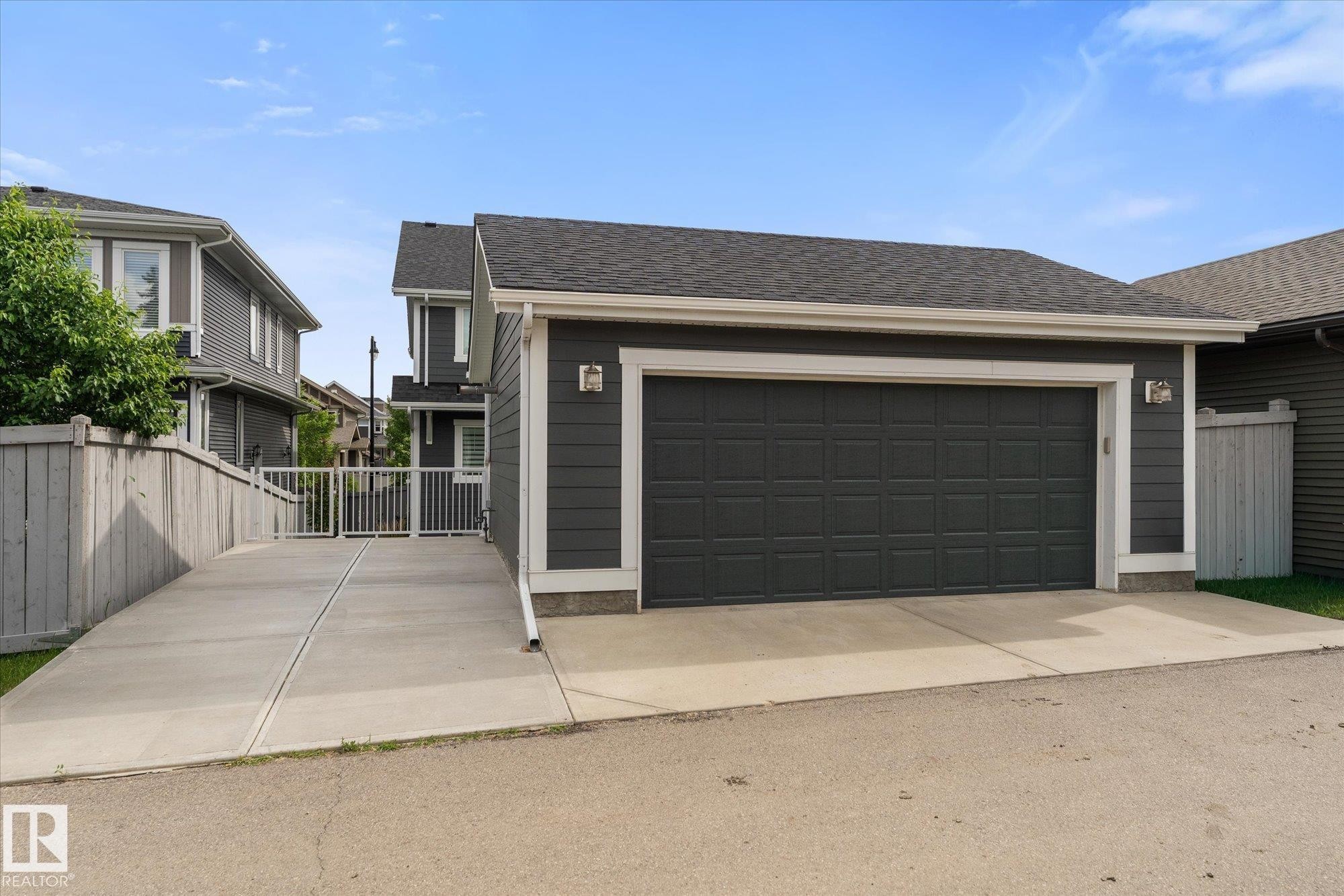 Spacious two-car garage with dark panel doors and concrete apron, complemented by a contemporary home featuring dark exterior siding with contrasting trim, pitched rooflines, and manicured landscaping visible along the property perimeter - 5616 Juchli Avenue Nw, Edmonton, AB - Outdoor