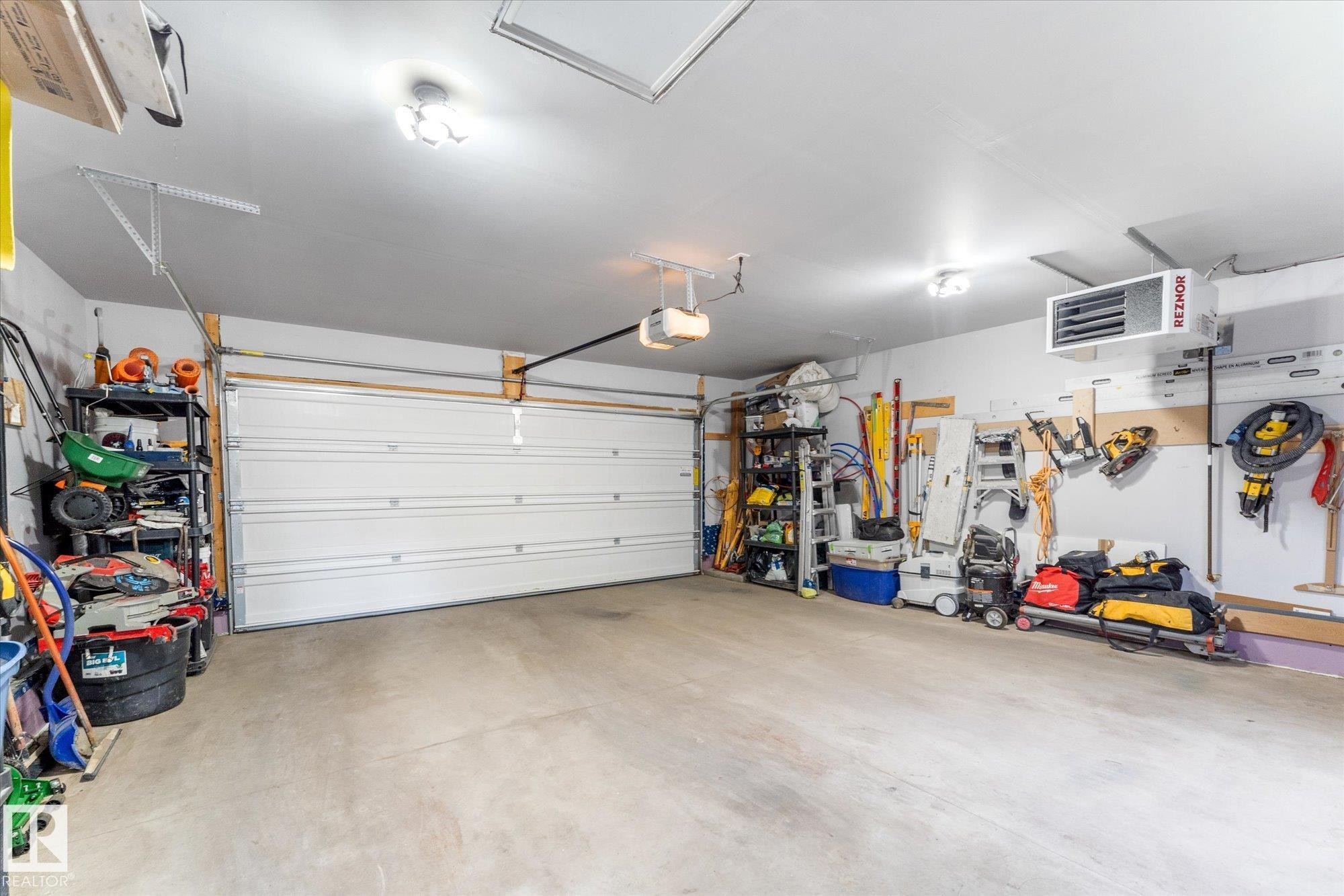 Attached garage with a white sectional door, overhead lighting, and built-in wall-mounted storage solutions - 5616 Juchli Avenue Nw, Edmonton, AB - Indoor Photo Showing Garage
