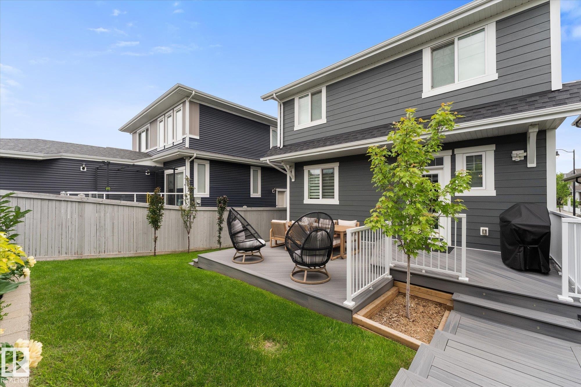 Rear exterior featuring a composite deck with white railings, a treed planter, and a green lawn area - 5616 Juchli Avenue Nw, Edmonton, AB - Outdoor With Deck Patio Veranda