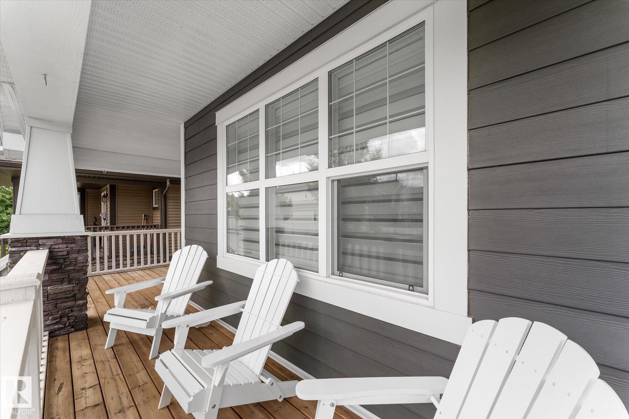 Expansive covered porch featuring a wood-finish floor, stone-clad pillar, white railing, and horizontal siding - 5616 Juchli Avenue Nw, Edmonton, AB - Outdoor With Deck Patio Veranda With Exterior
