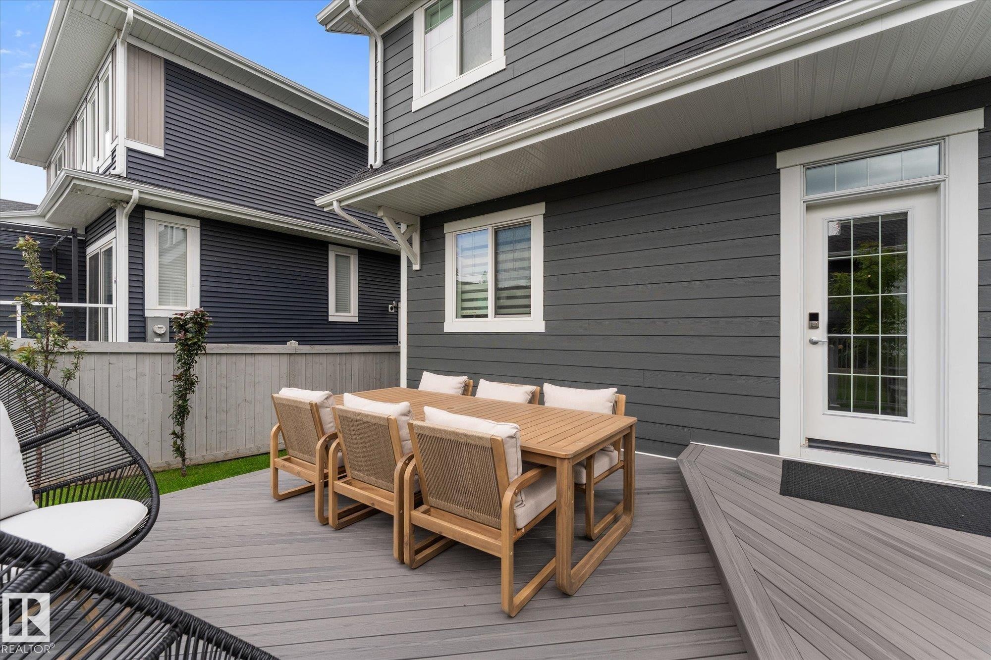 Expansive composite deck, white trim windows, white exterior door with transom, and dark gray horizontal siding - 5616 Juchli Avenue Nw, Edmonton, AB - Outdoor With Deck Patio Veranda With Exterior