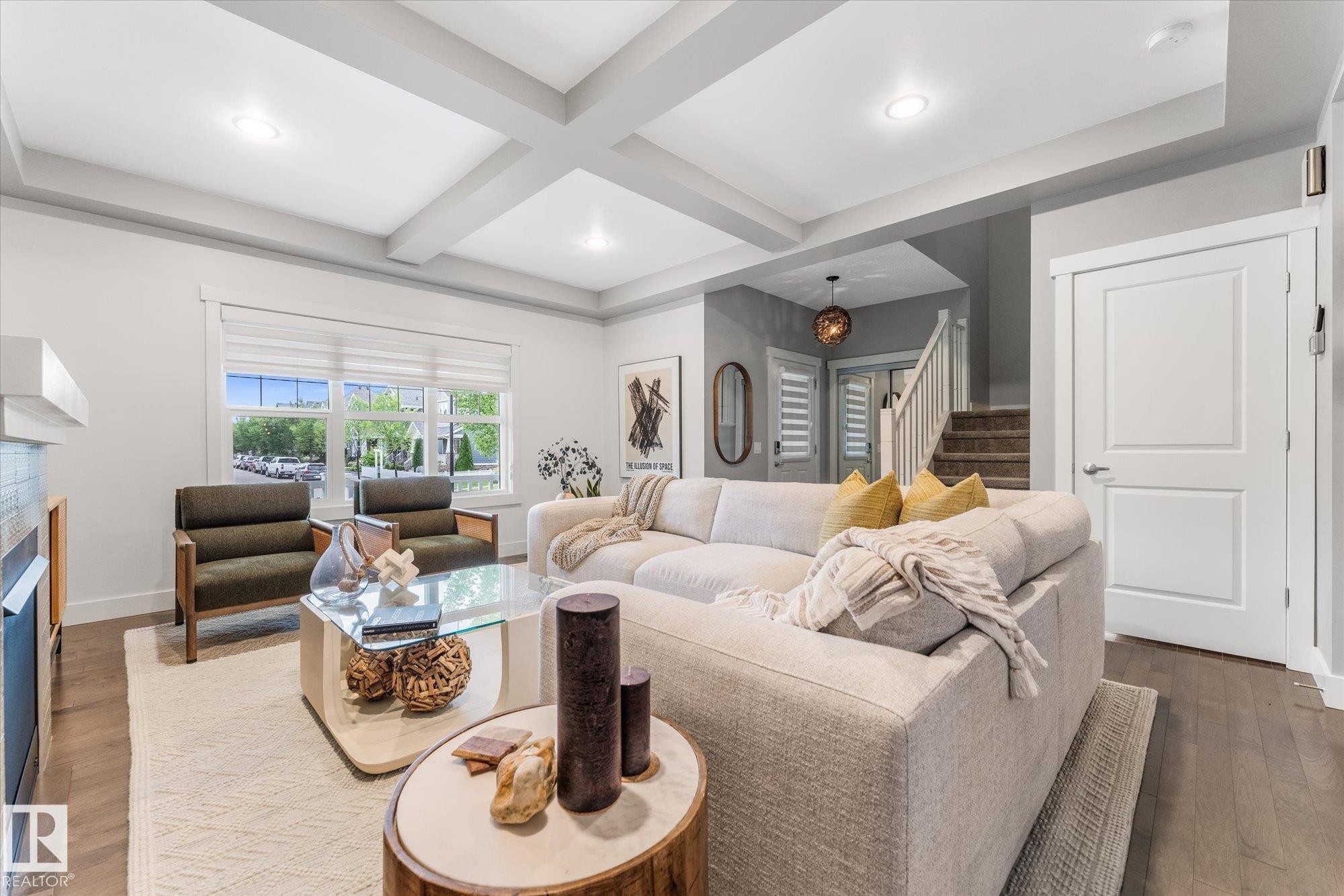 Sophisticated living room showcasing a coffered ceiling with recessed lighting, large multi-pane windows flooding the space with natural light, and wood-finish flooring throughout - 5616 Juchli Avenue Nw, Edmonton, AB - Indoor Photo Showing Living Room