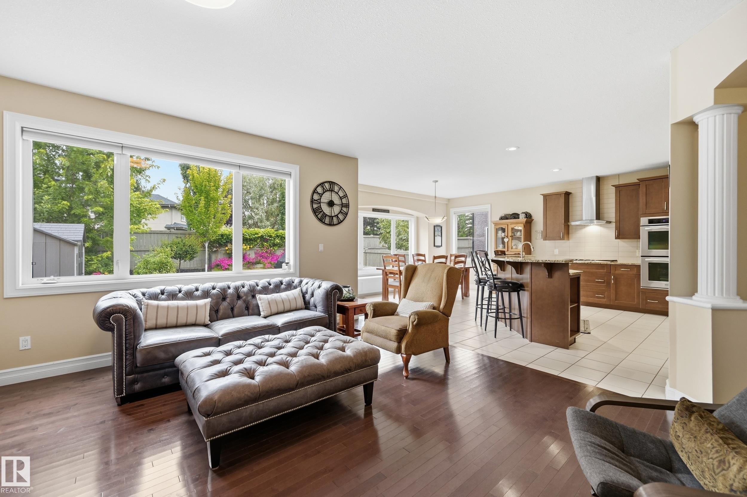 Hardwood-finish flooring throughout, large window with expansive glass panes, kitchen island with seating, stainless steel appliances, and a decorative column - 2416 Warry Place Sw, Edmonton, AB - Indoor Photo Showing Living Room