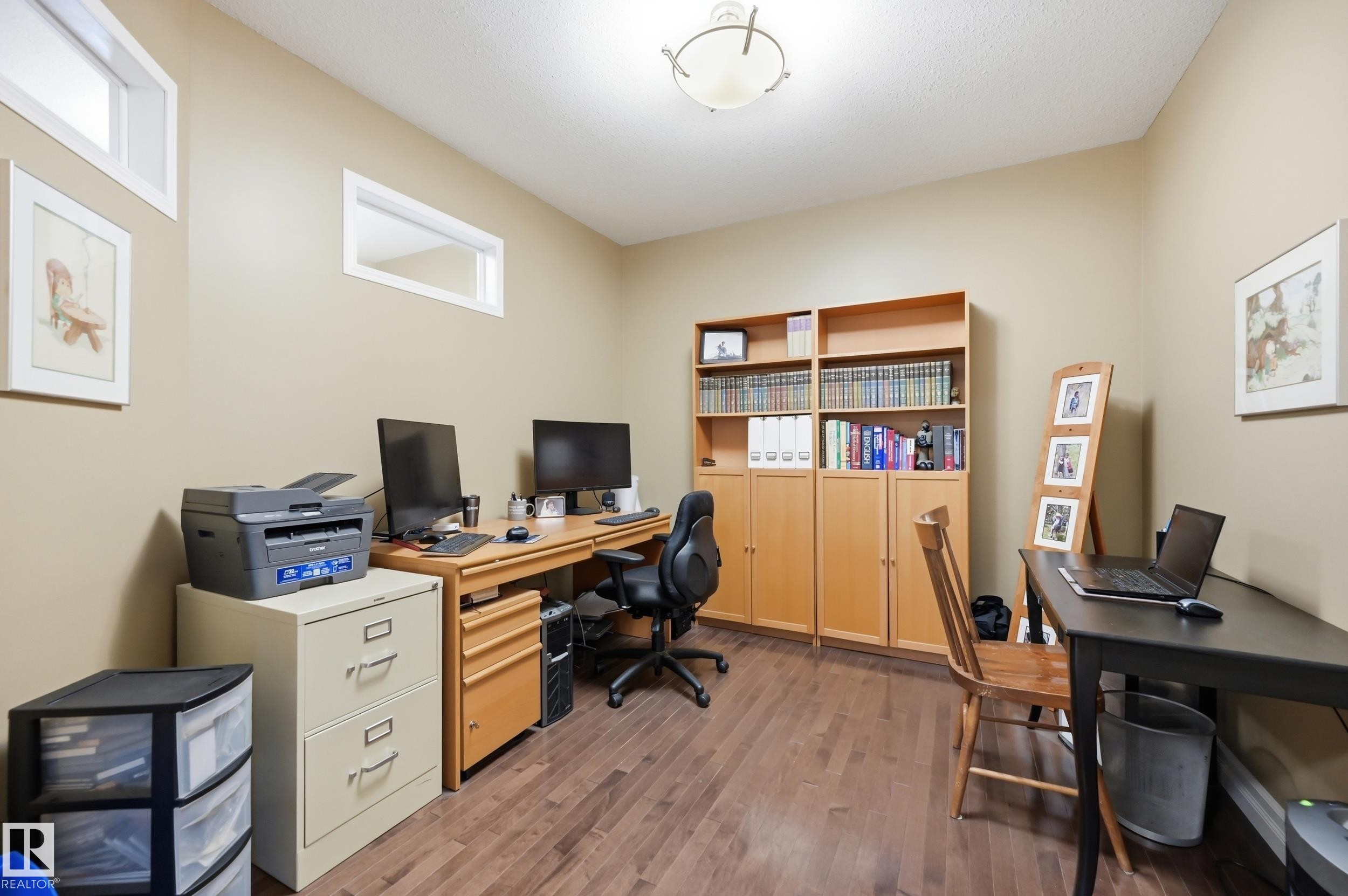 Wood-finish flooring, built-in shelving, two transom windows, and a flush mount ceiling light fixture - 2416 Warry Place Sw, Edmonton, AB - Indoor Photo Showing Office