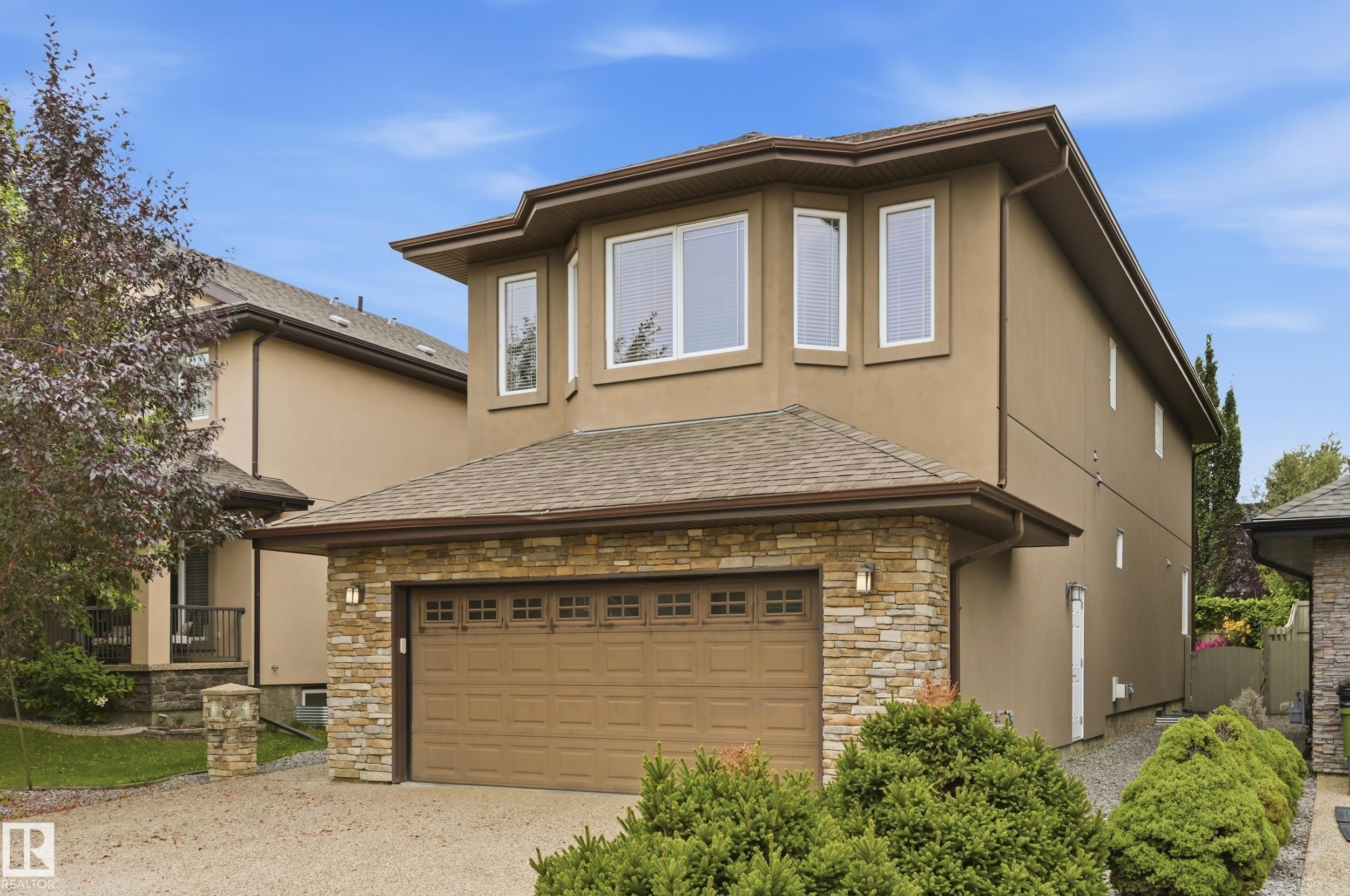 Stucco exterior with stone accents, attached two-car garage, multiple upper-level windows, and a shingled roof - 2416 Warry Place Sw, Edmonton, AB - Outdoor With Exterior