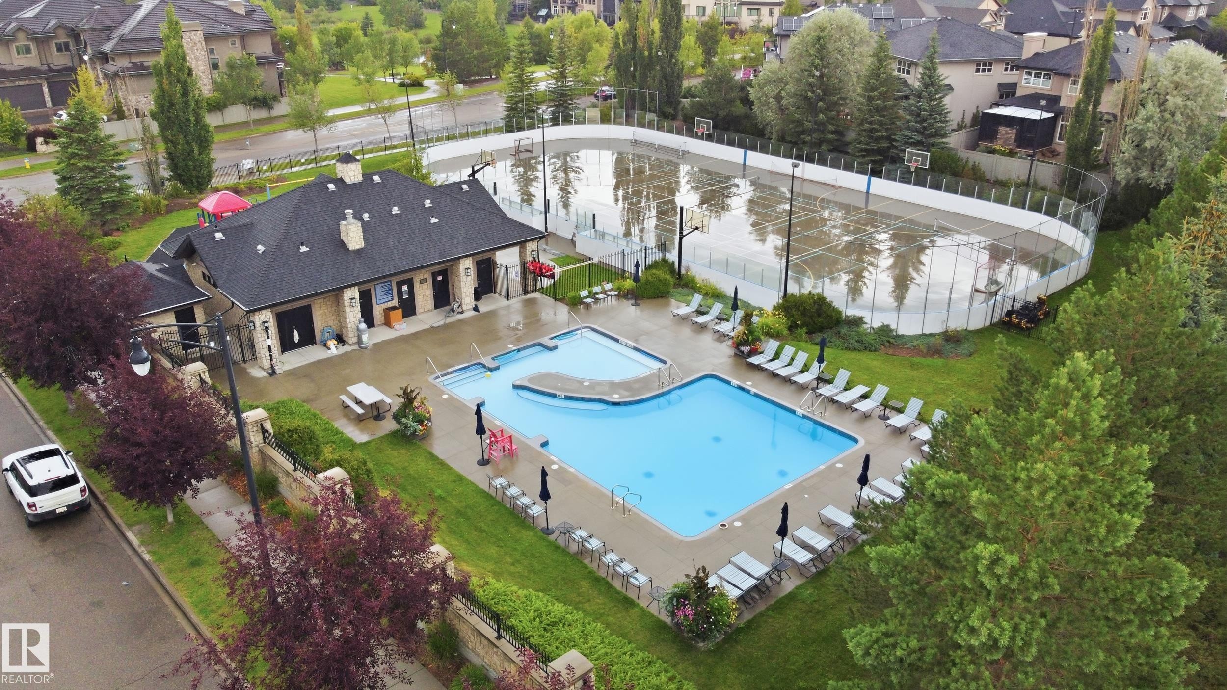 Community clubhouse building with a dark shingle roof, a large outdoor swimming pool, and an adjacent multi-sport court - 2416 Warry Place Sw, Edmonton, AB - Outdoor With In Ground Pool With Deck Patio Veranda With View