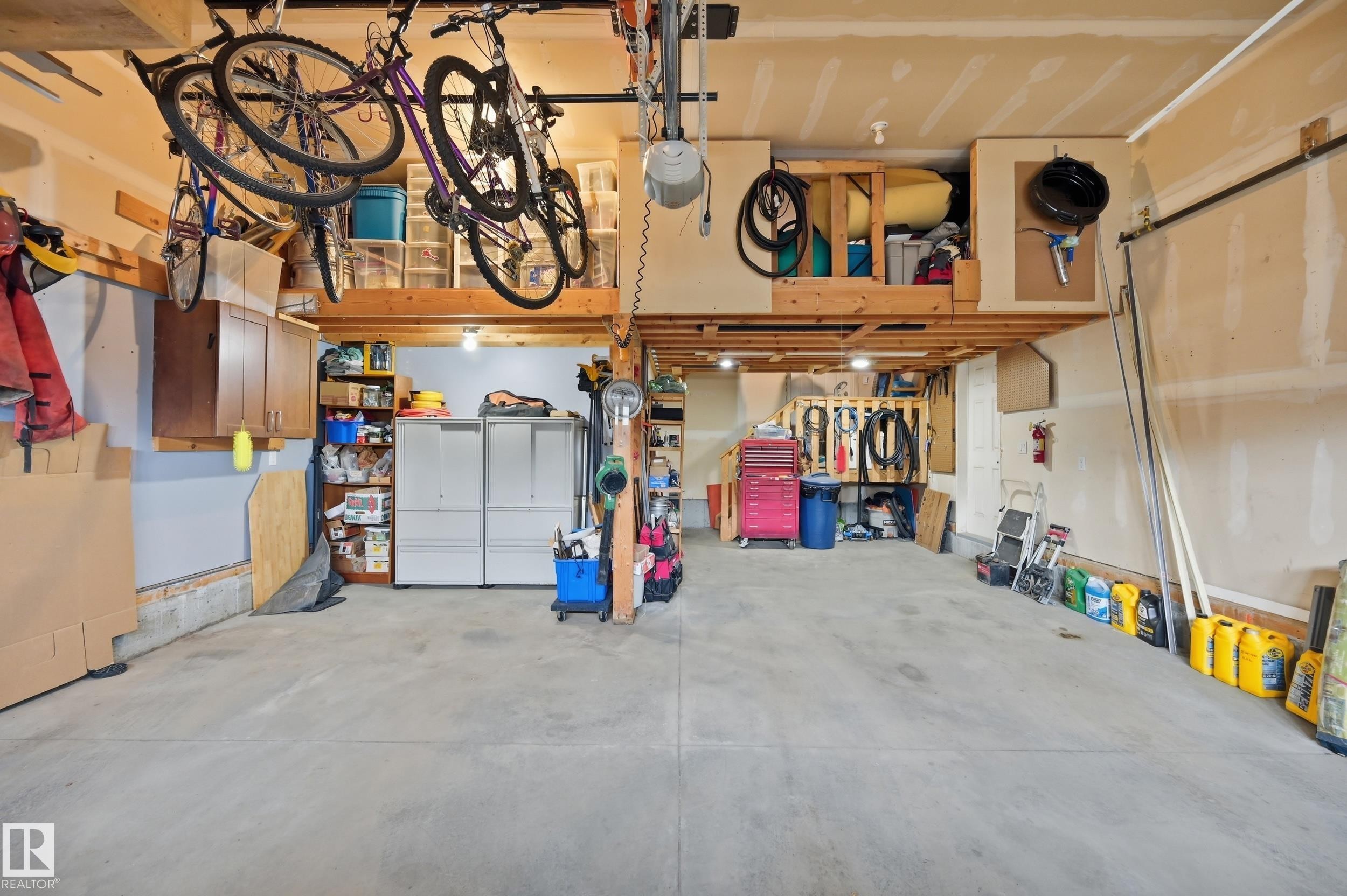 Finished concrete flooring, exposed wood beam ceiling, built-in storage shelving, and overhead storage platforms - 2416 Warry Place Sw, Edmonton, AB - Indoor Photo Showing Garage