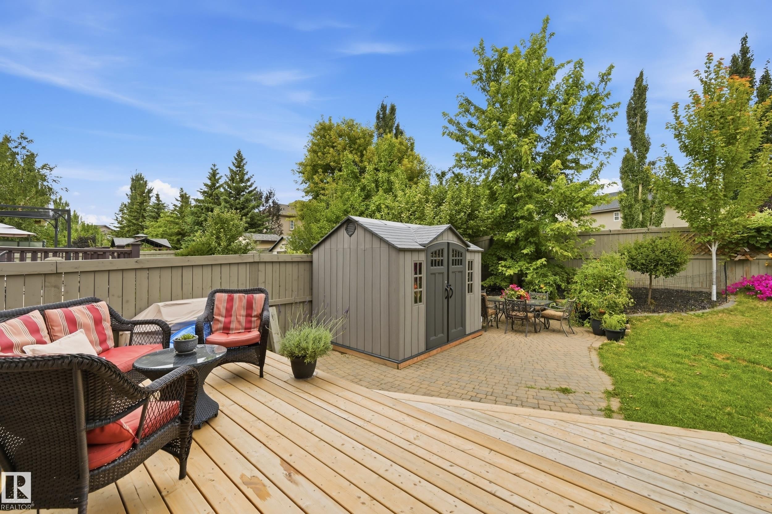 Expansive wood deck with a privacy fence, leading to a paver patio and lawn area with mature trees and a storage shed - 2416 Warry Place Sw, Edmonton, AB - Outdoor With Deck Patio Veranda