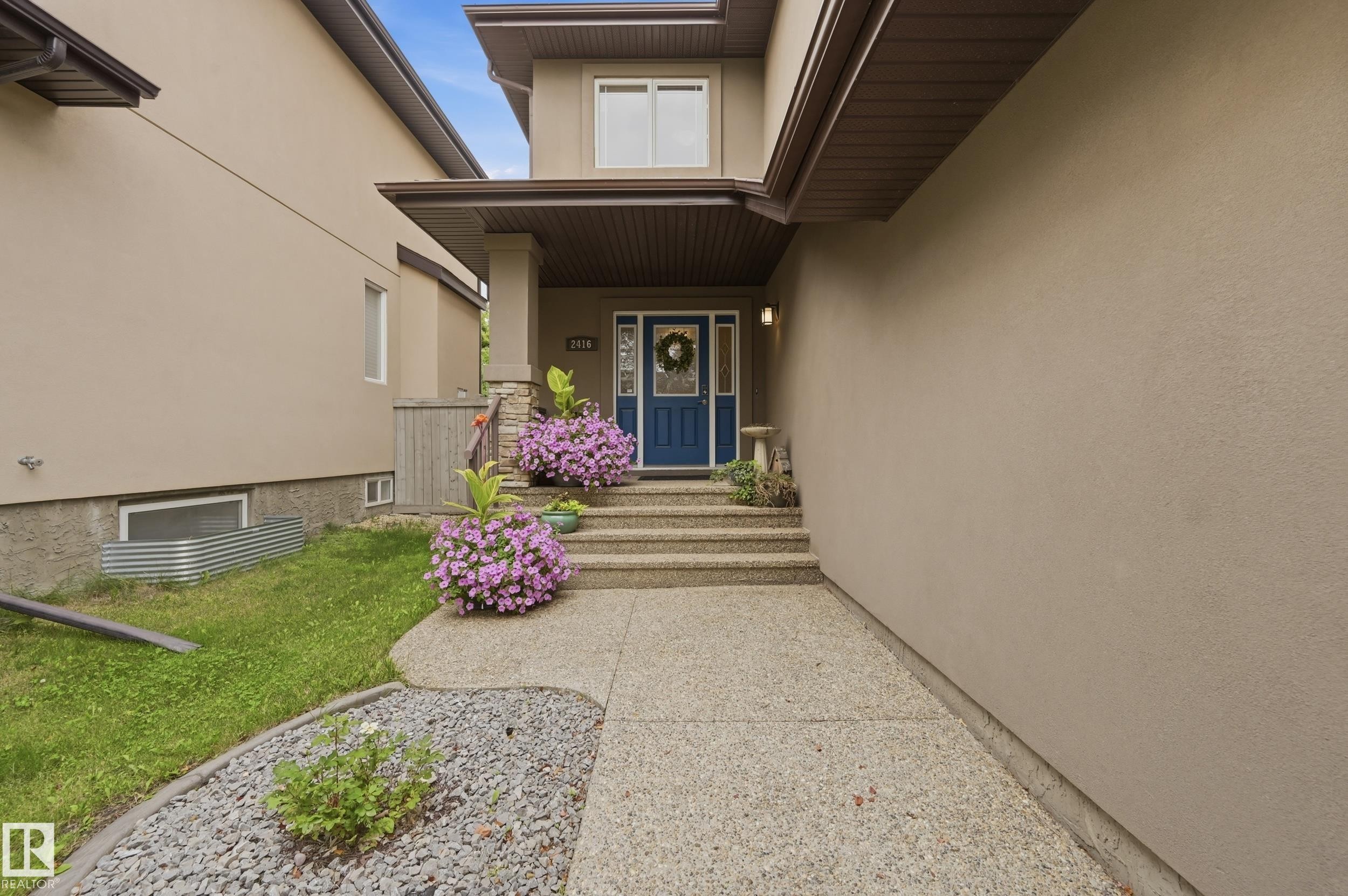 Stucco exterior with a blue entry door, concrete steps, and an exposed aggregate walkway - 2416 Warry Place Sw, Edmonton, AB - Outdoor With Deck Patio Veranda