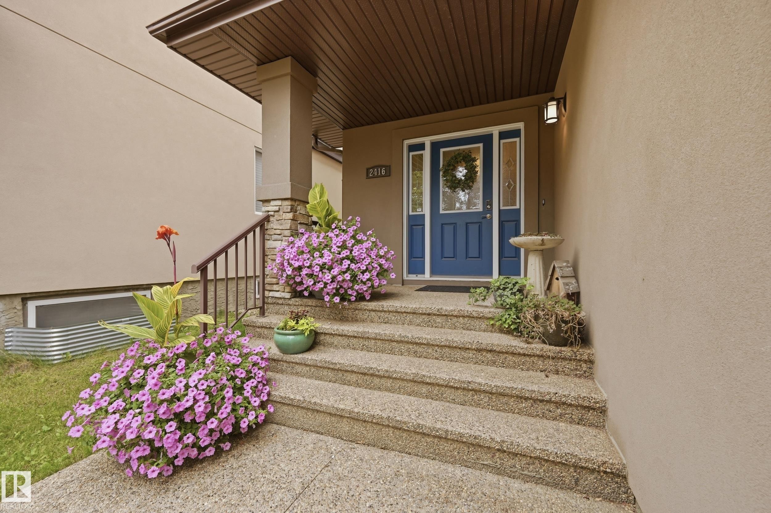 Blue entry door with side lites, exposed aggregate concrete steps, and a stone-clad porch column - 2416 Warry Place Sw, Edmonton, AB - Outdoor With Deck Patio Veranda