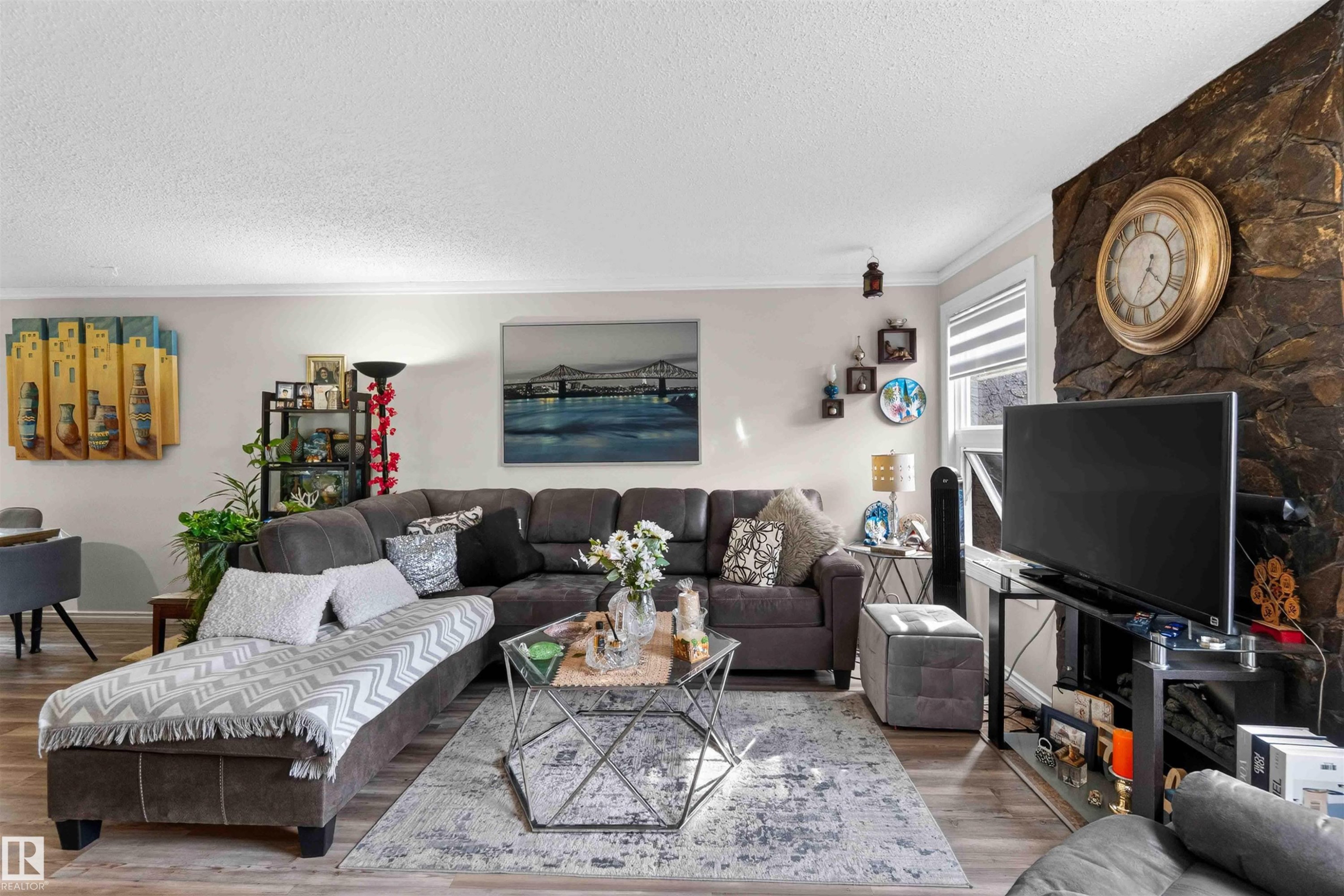 Living area featuring wood-finish flooring, a stacked stone accent wall, and crown molding - 17127 109 Street Nw, Edmonton, AB - Indoor Photo Showing Living Room