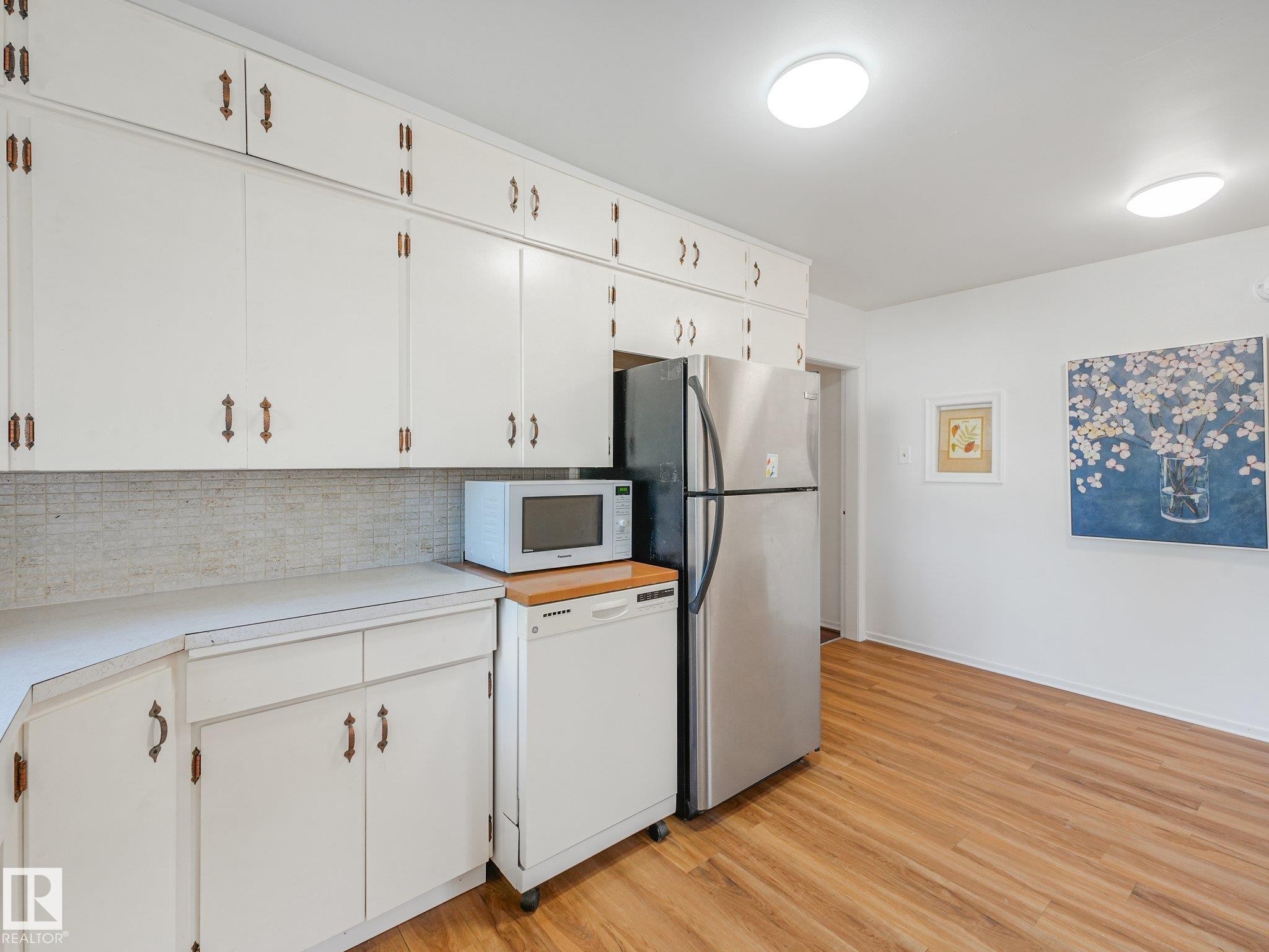 White cabinetry with decorative hardware, light-toned backsplash, and wood-finish flooring - 6112 105A Street Nw, Edmonton, AB - Indoor Photo Showing Kitchen