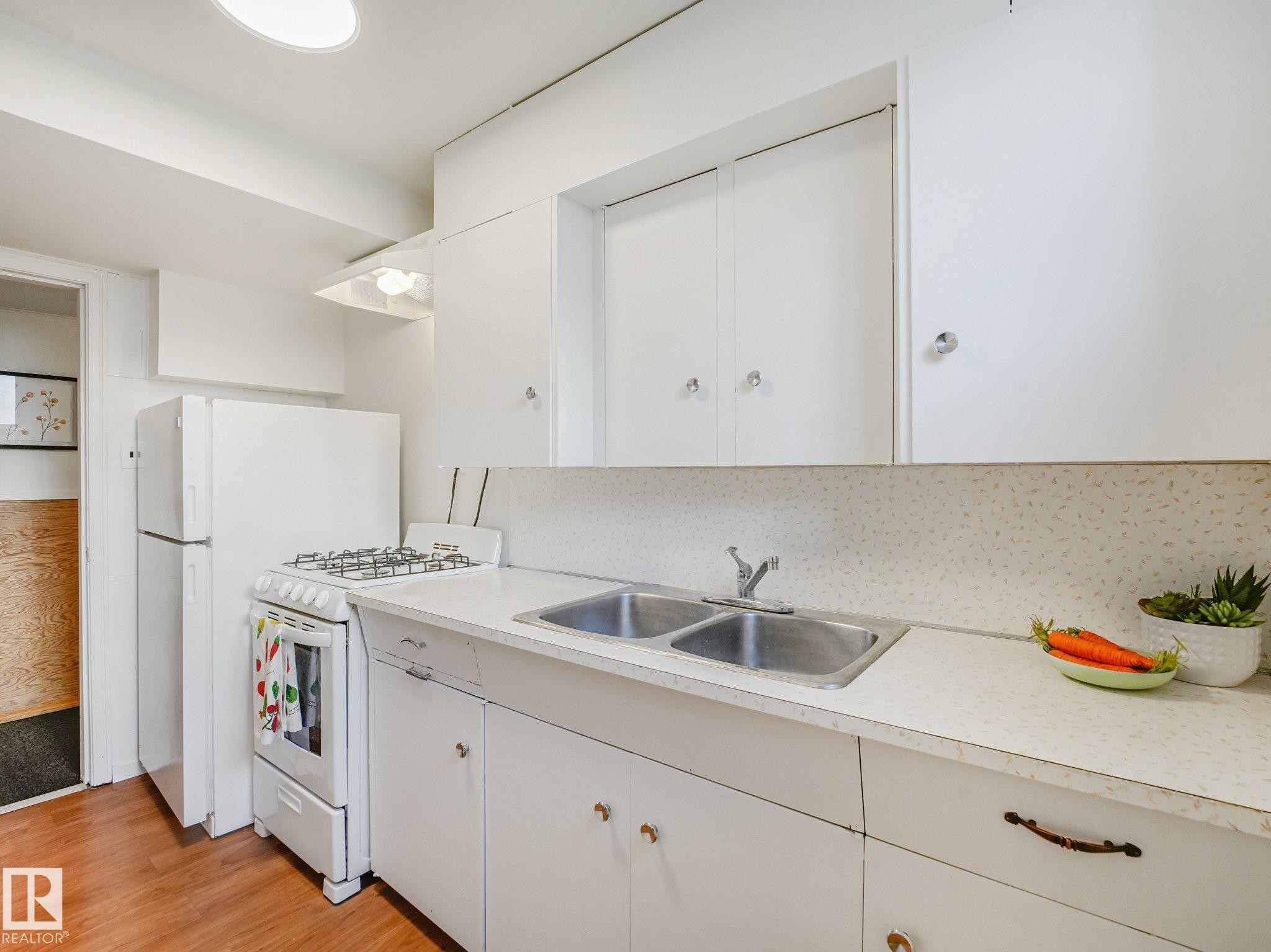 White cabinetry and countertops, with a dual-basin stainless steel sink, and wood-finish flooring - 6112 105A Street Nw, Edmonton, AB - Indoor Photo Showing Kitchen With Double Sink