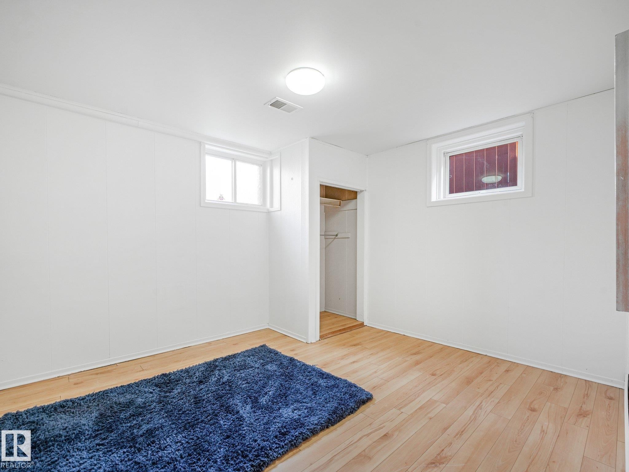 Wood-finish flooring, white paneled walls, two windows, and an open closet with shelving - 6112 105A Street Nw, Edmonton, AB - Indoor Photo Showing Other Room