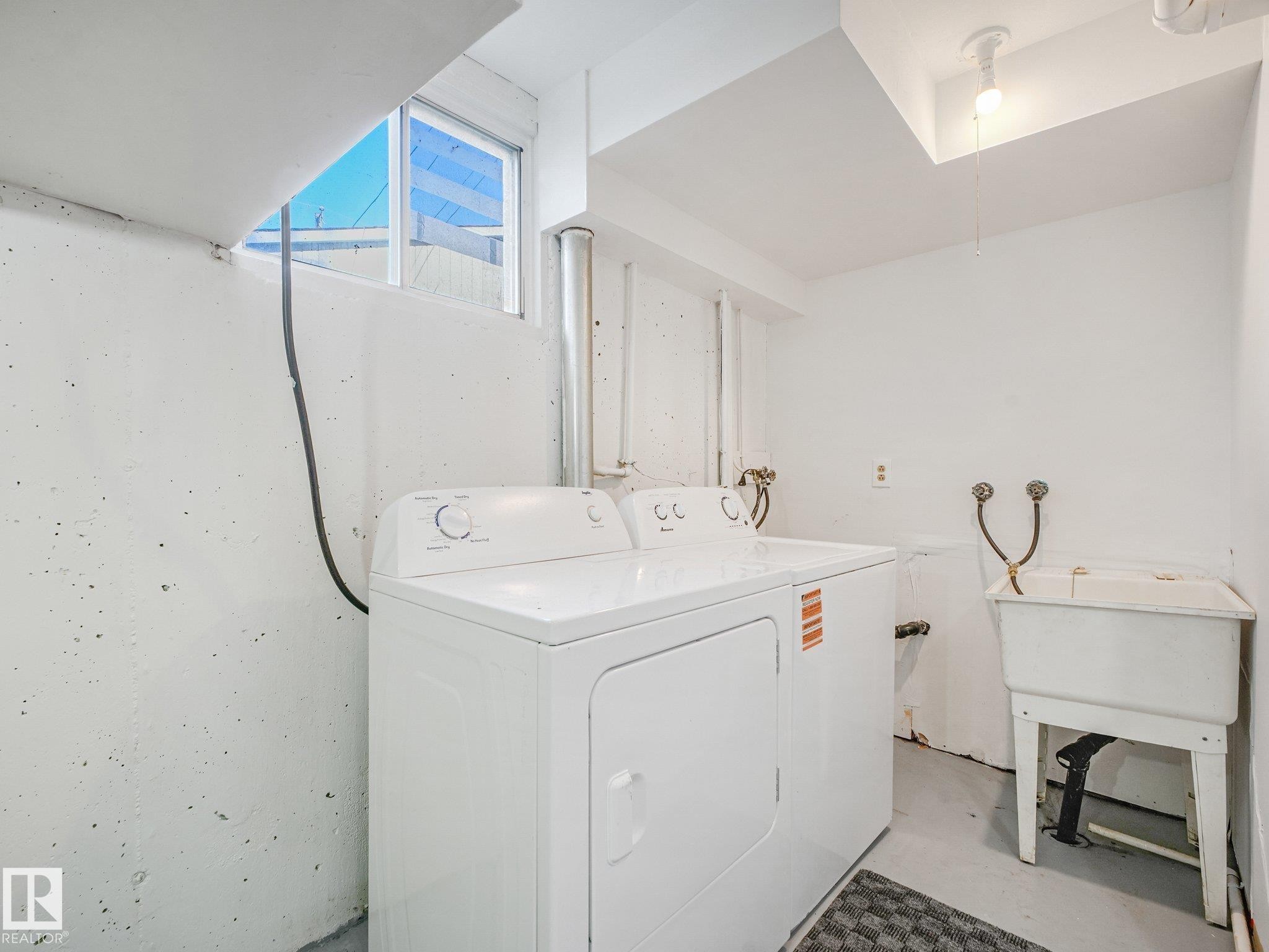 Dedicated laundry area featuring a utility sink, large window, and overhead lighting - 6112 105A Street Nw, Edmonton, AB - Indoor Photo Showing Laundry Room