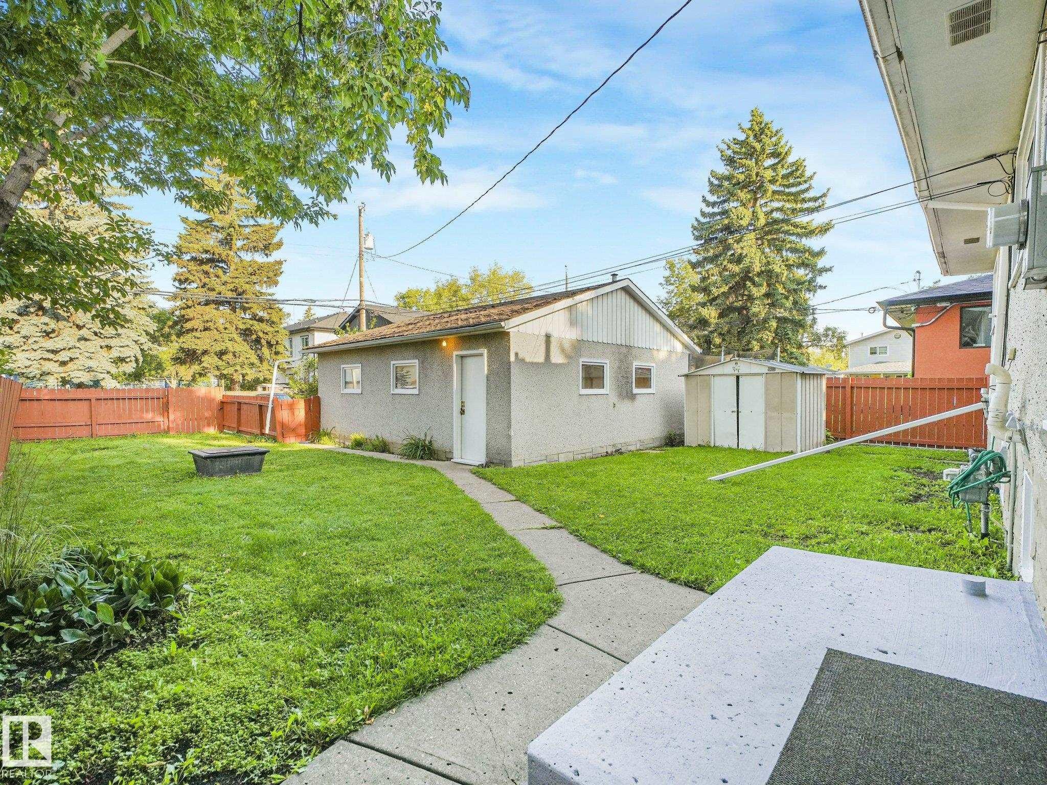 Expansive backyard featuring a concrete patio, established trees, and a detached structure with a concrete pathway - 6112 105A Street Nw, Edmonton, AB - Outdoor