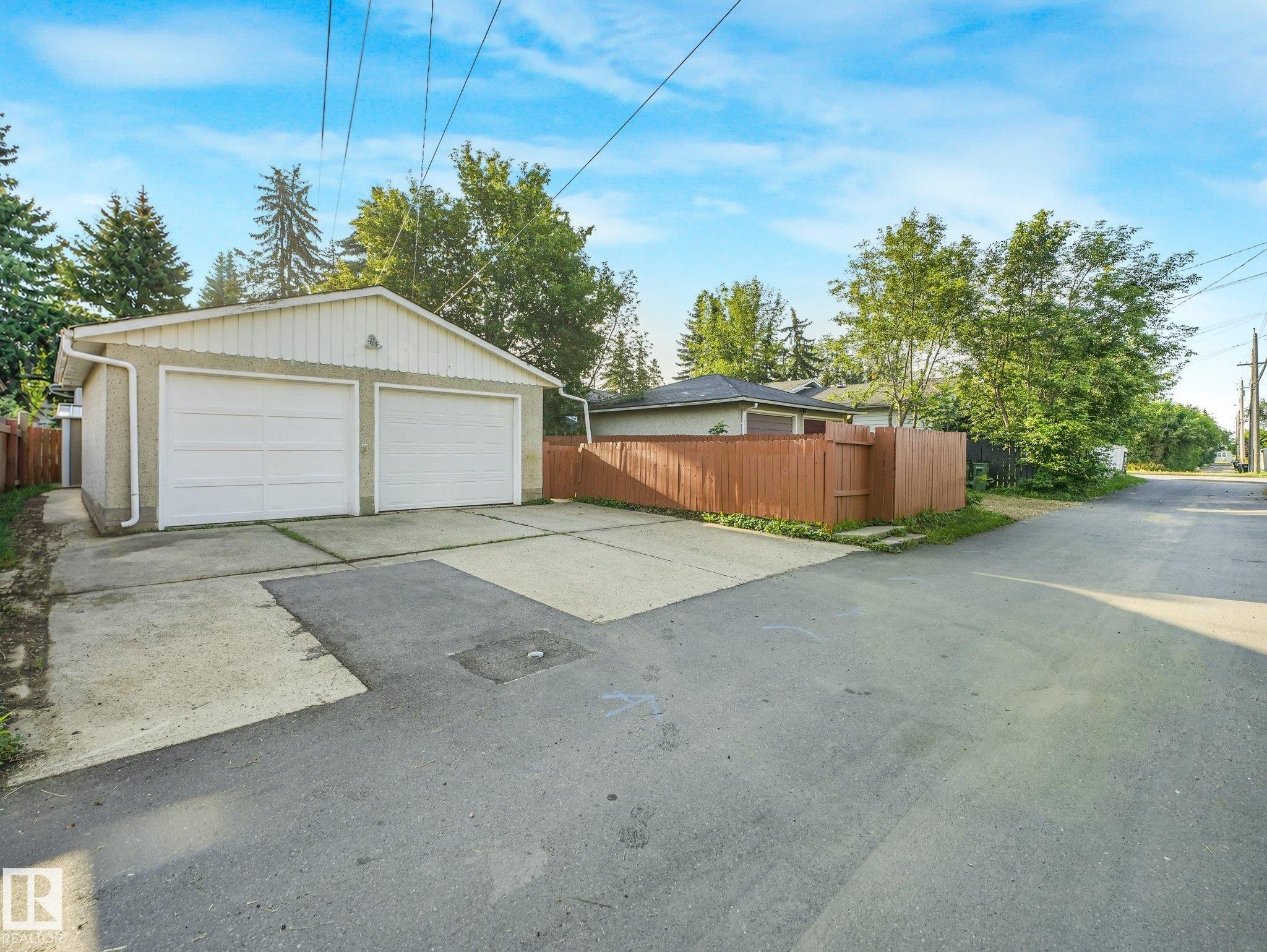 Detached two-car garage with two white panel garage doors, concrete driveway, and brown privacy fencing - 6112 105A Street Nw, Edmonton, AB - Outdoor