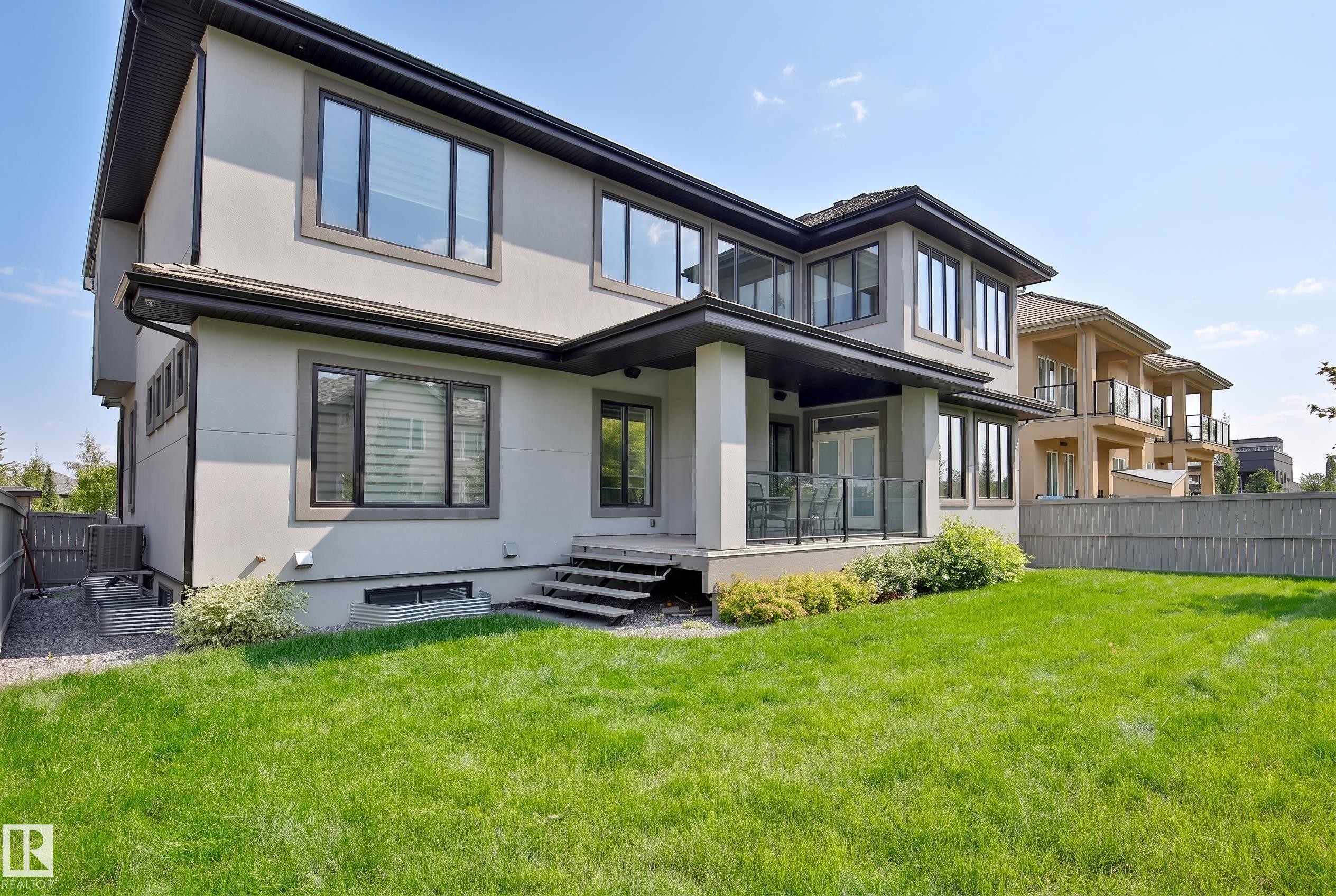 Stucco exterior with dark trim windows, covered outdoor patio space, glass panel railings, and a manicured lawn area - 3644 Westcliff Way Sw, Edmonton, AB - Outdoor With Deck Patio Veranda