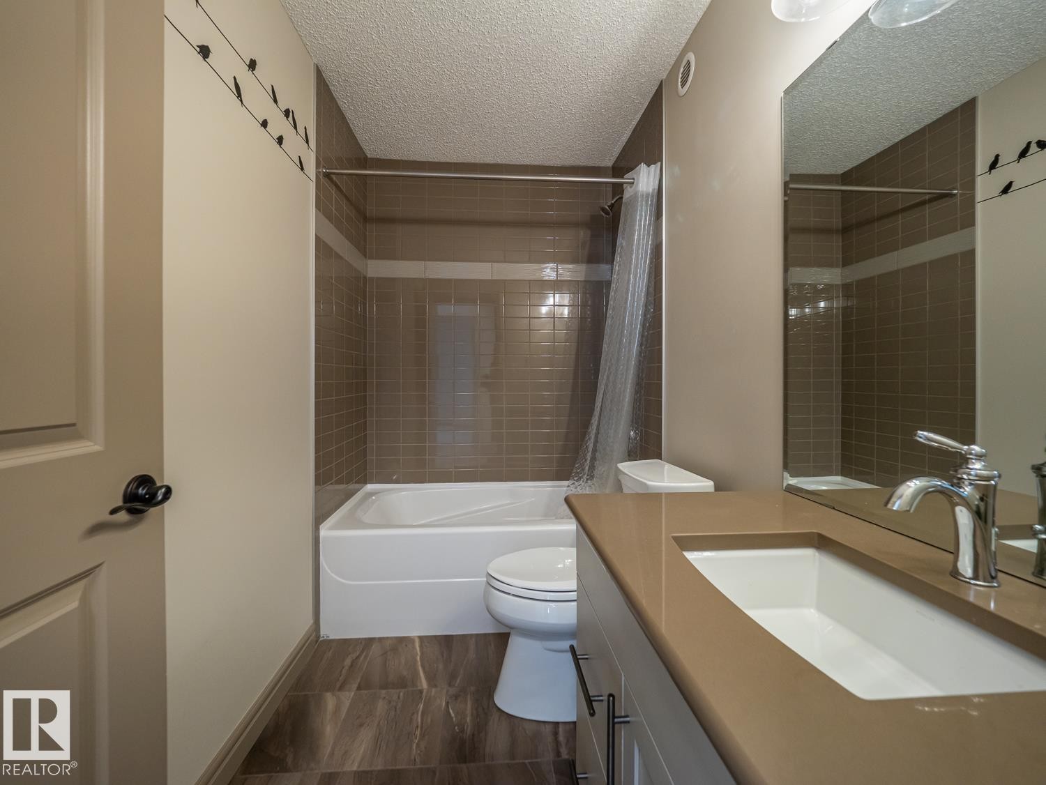 Integrated bathtub with shower, brown tile surround, wood-finish flooring, vanity with integrated sink and countertop, and a large wall-mounted mirror - 97 Astoria Point(E), Devon, AB - Indoor Photo Showing Bathroom