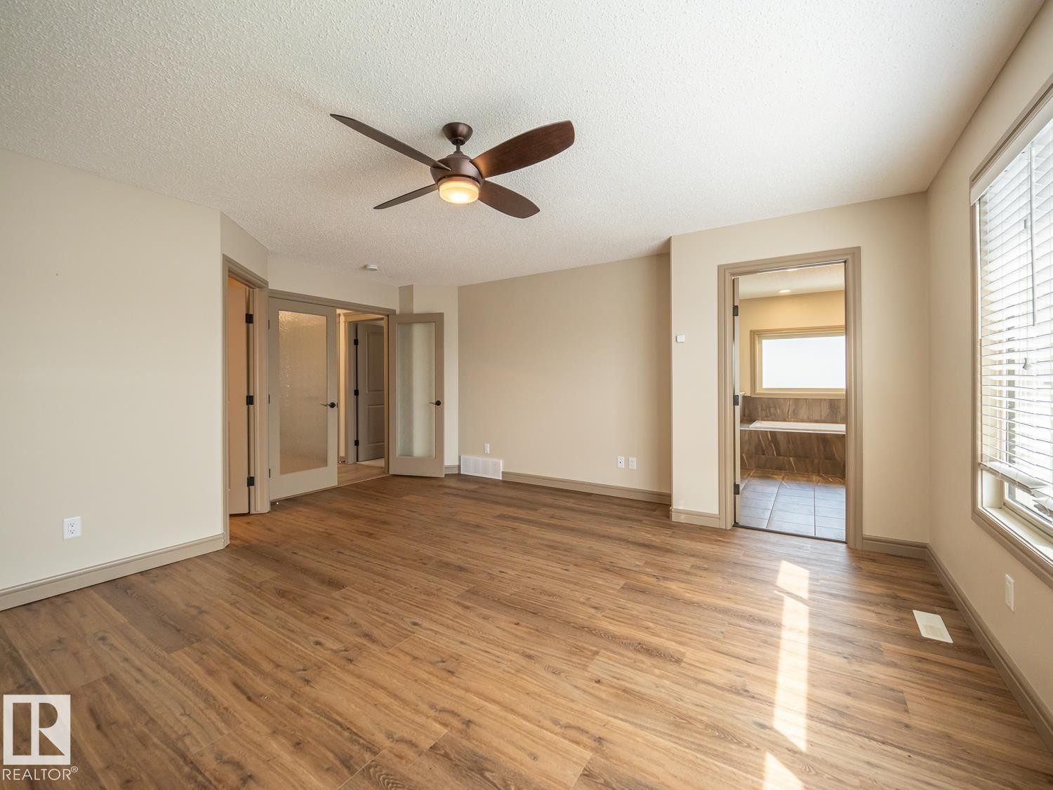 Wood-finish flooring, ceiling fan, neutral wall tones, large window with blinds, and double French doors with frosted glass - 97 Astoria Point(E), Devon, AB - Indoor Photo Showing Other Room