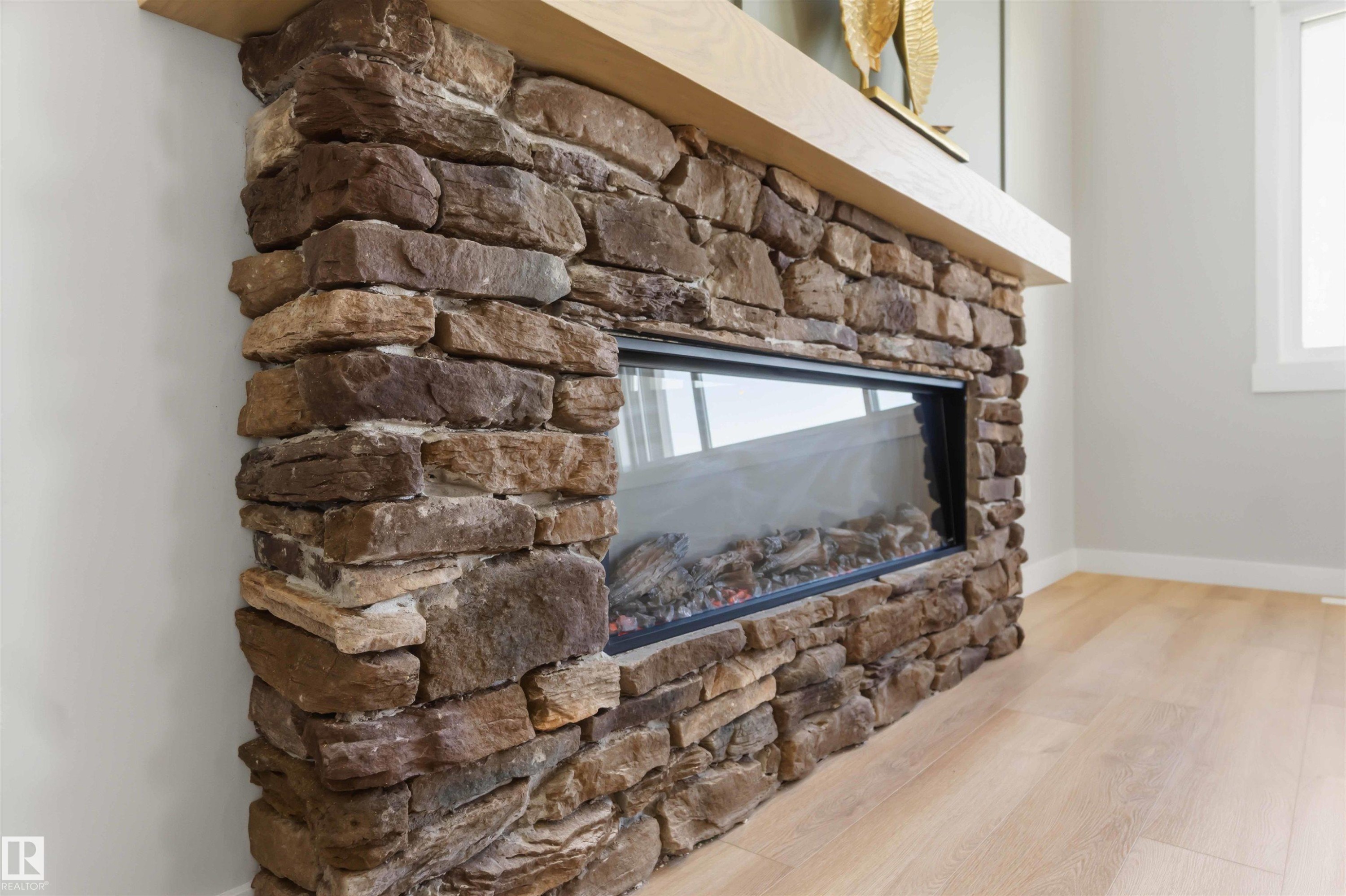 Stone-clad fireplace featuring a linear electric insert and a light wood mantel - 28 Harley Way, Spruce Grove, AB - Indoor Photo Showing Living Room With Fireplace
