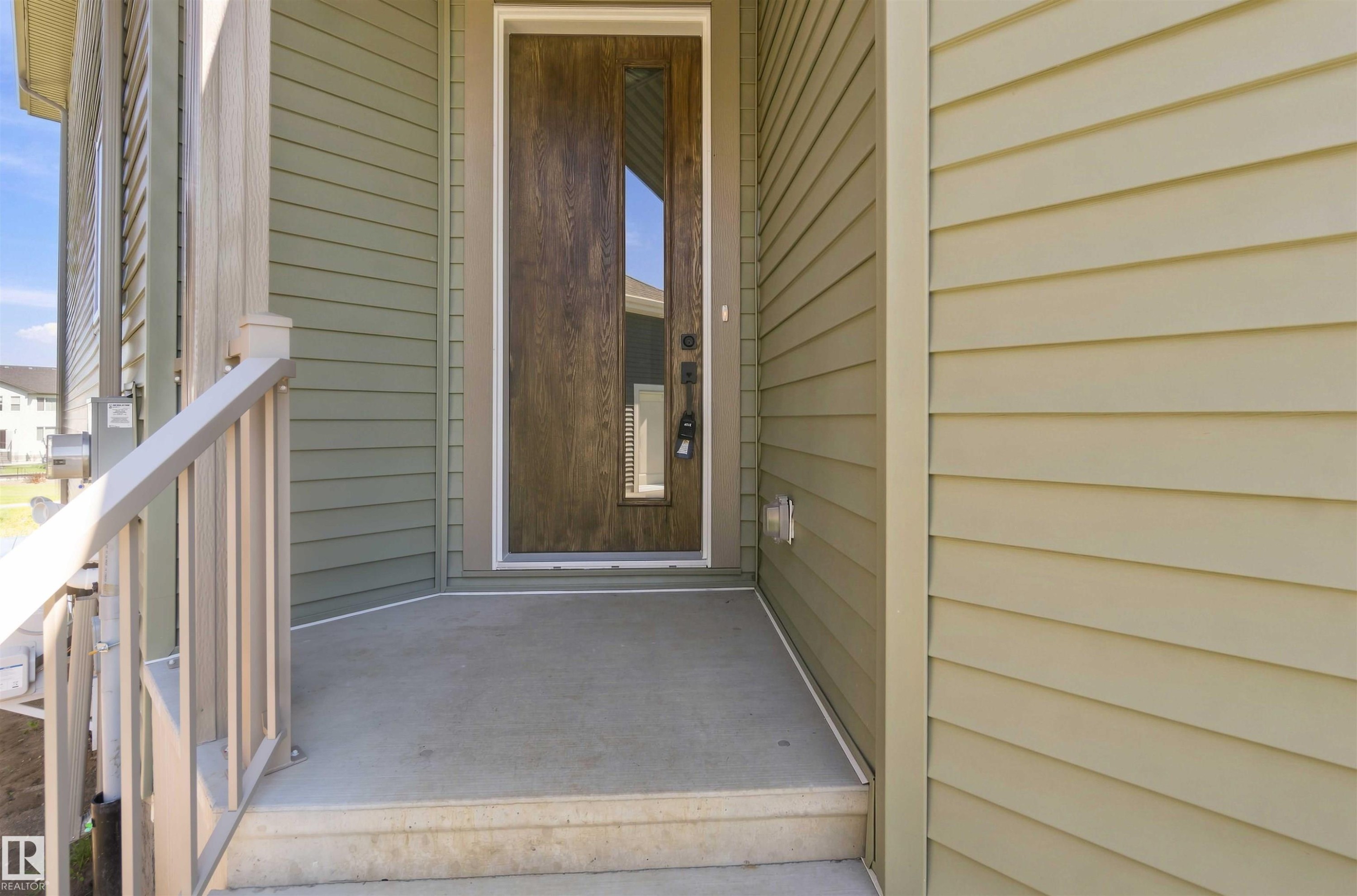 Wood-finish entry door with vertical window inset, concrete porch and steps, composite railing, and horizontal siding in two tones - 28 Harley Way, Spruce Grove, AB - Outdoor With Exterior